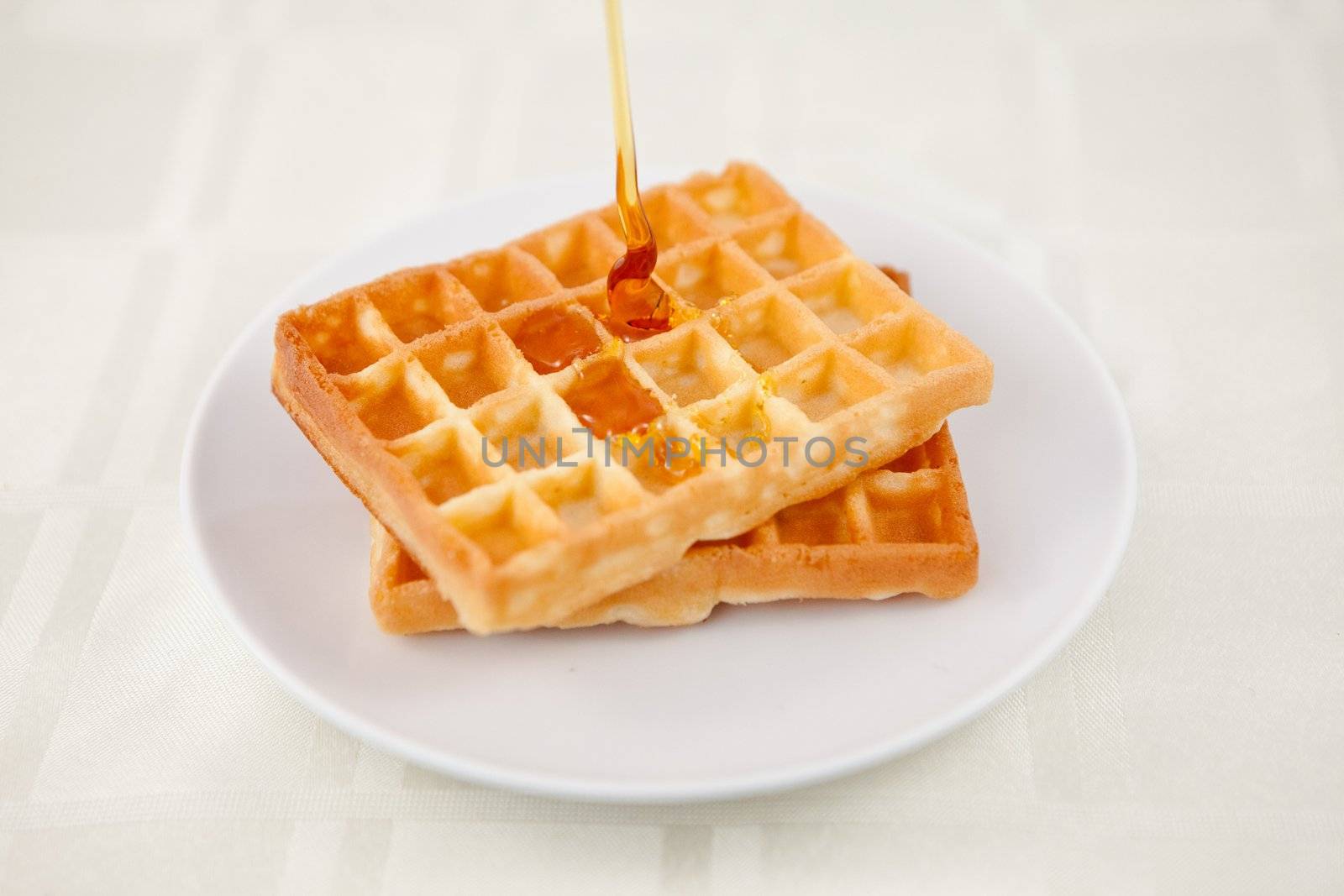 Honey falling on a waffle on a table