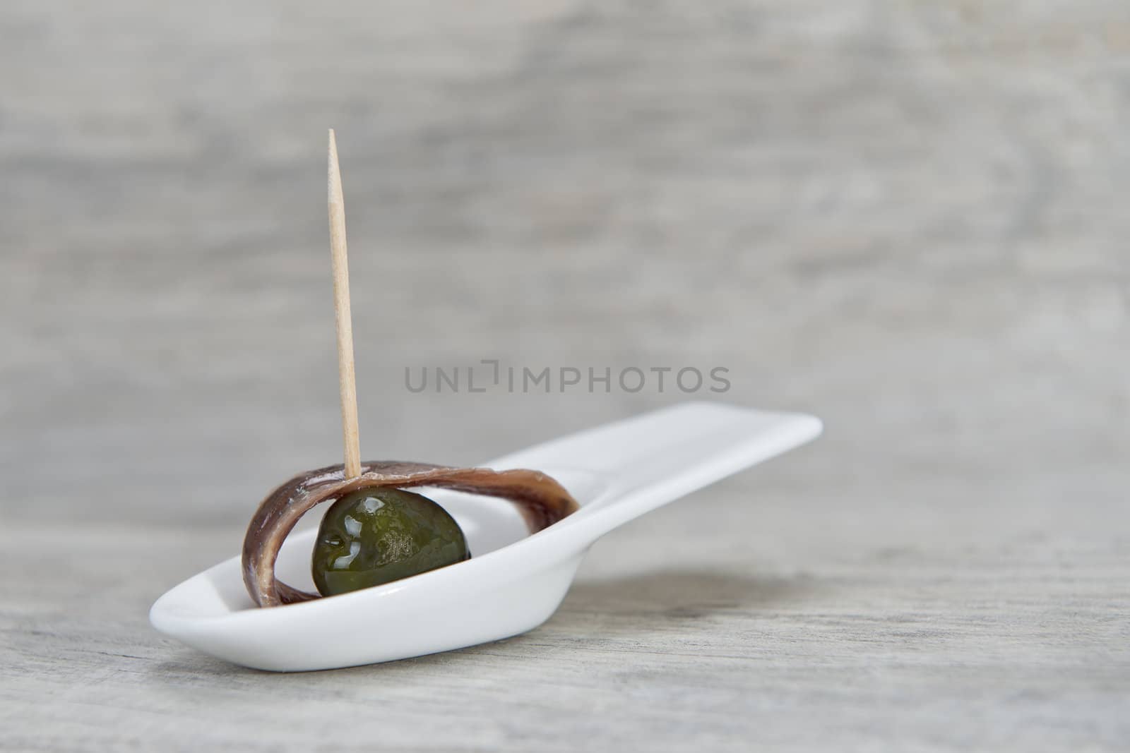 Anchovy appetizer served with green olives in a china spoon on a wooden background