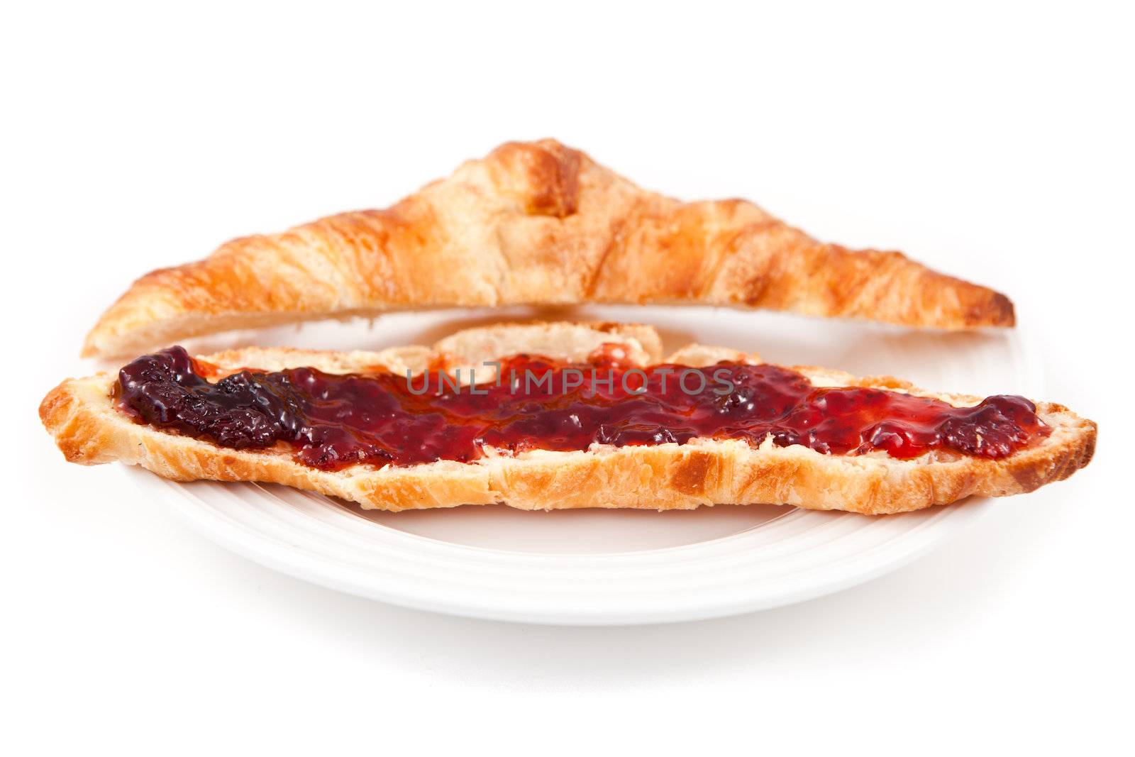 Croissant spread with jam in a plateful against white background