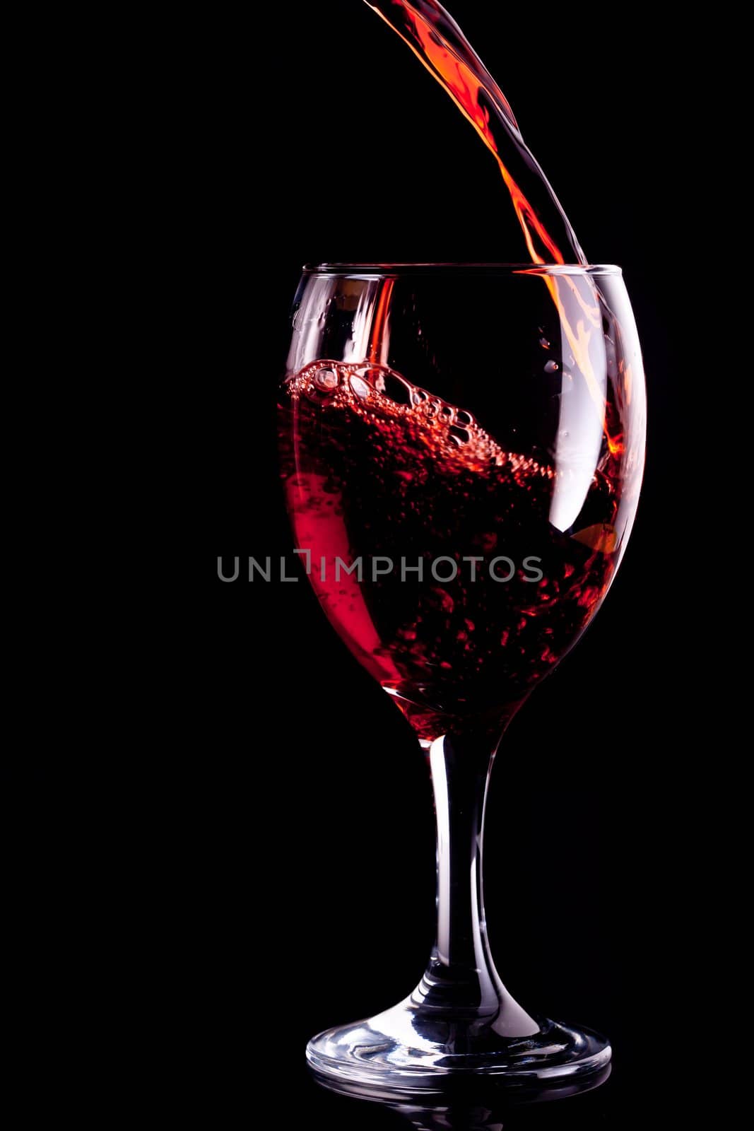Red wine being poured into glass against black background
