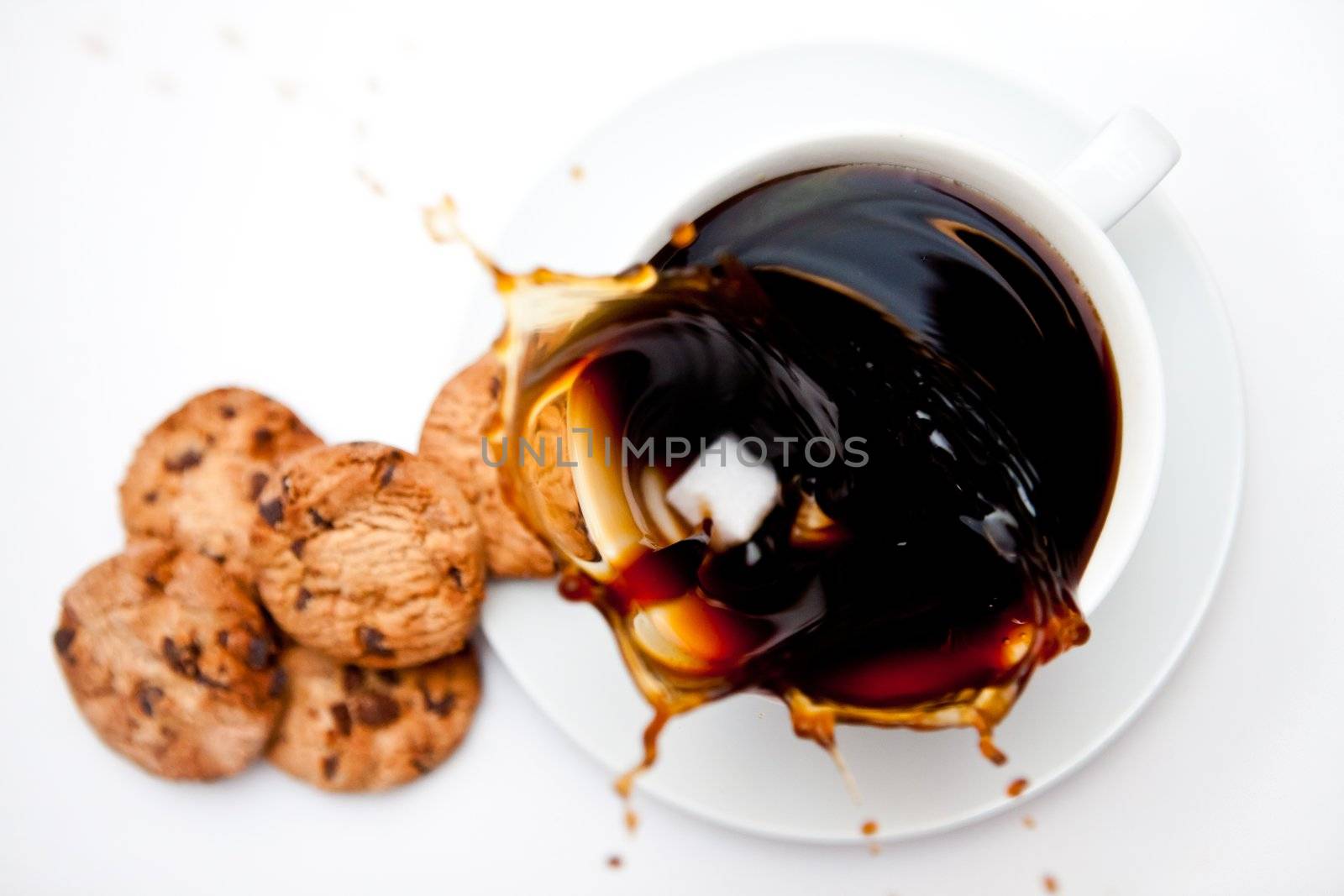 Sugar dropping in a cup of coffee with cookies against a white background