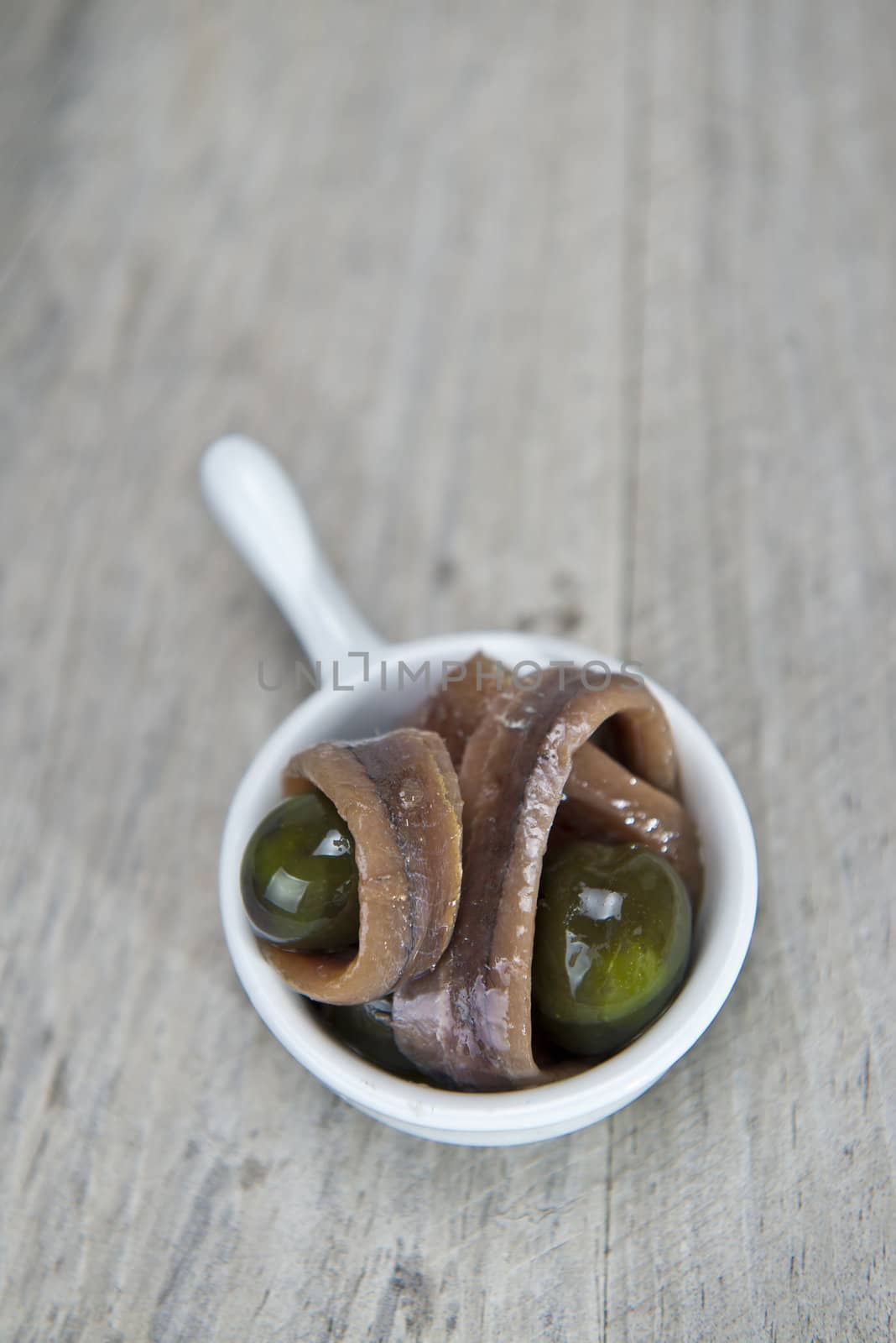 Anchovy appetizer served with green olives in a china spoon on a wooden background