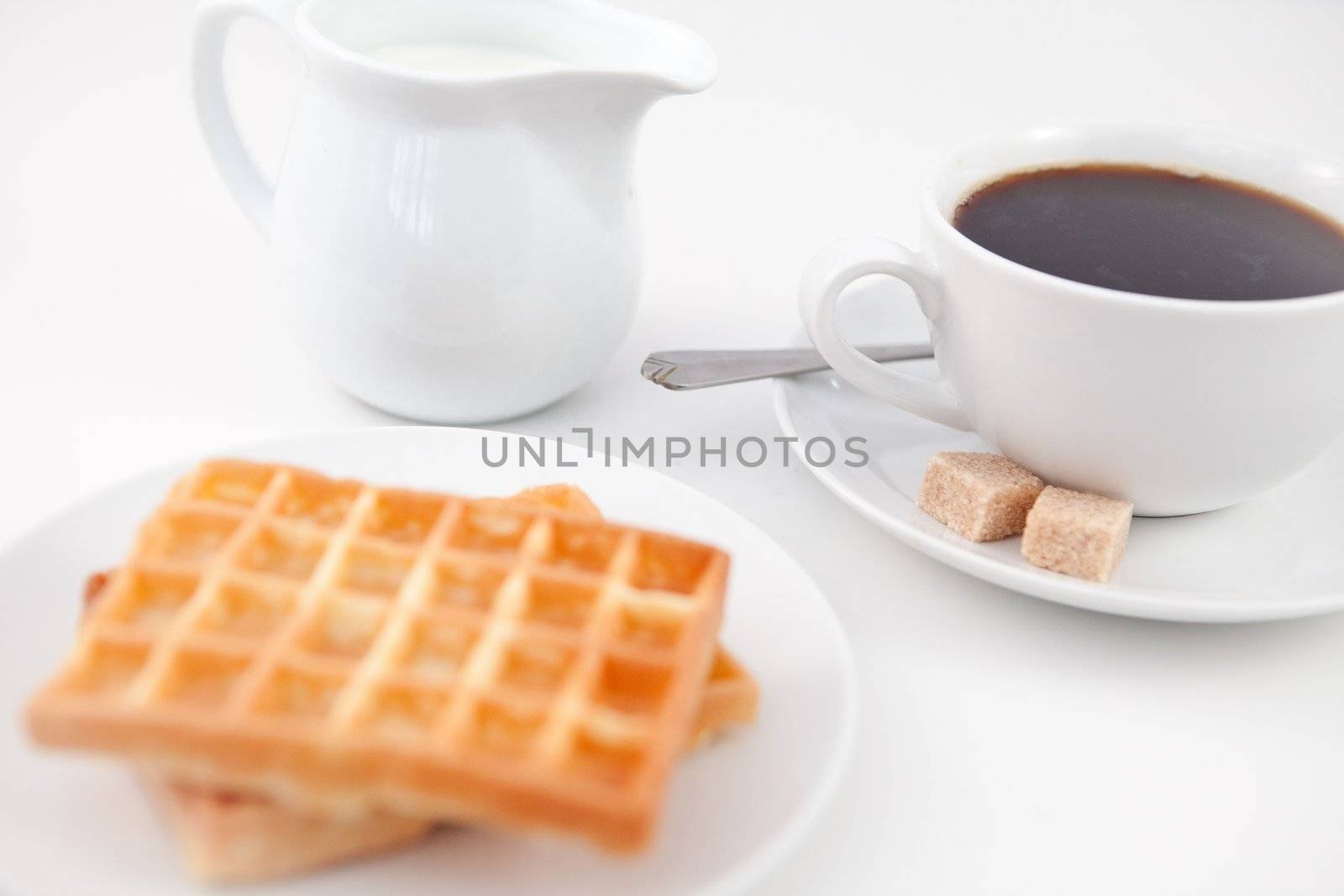 Waffles sugar milk and a cup of coffee on white plate with spoon against a white background