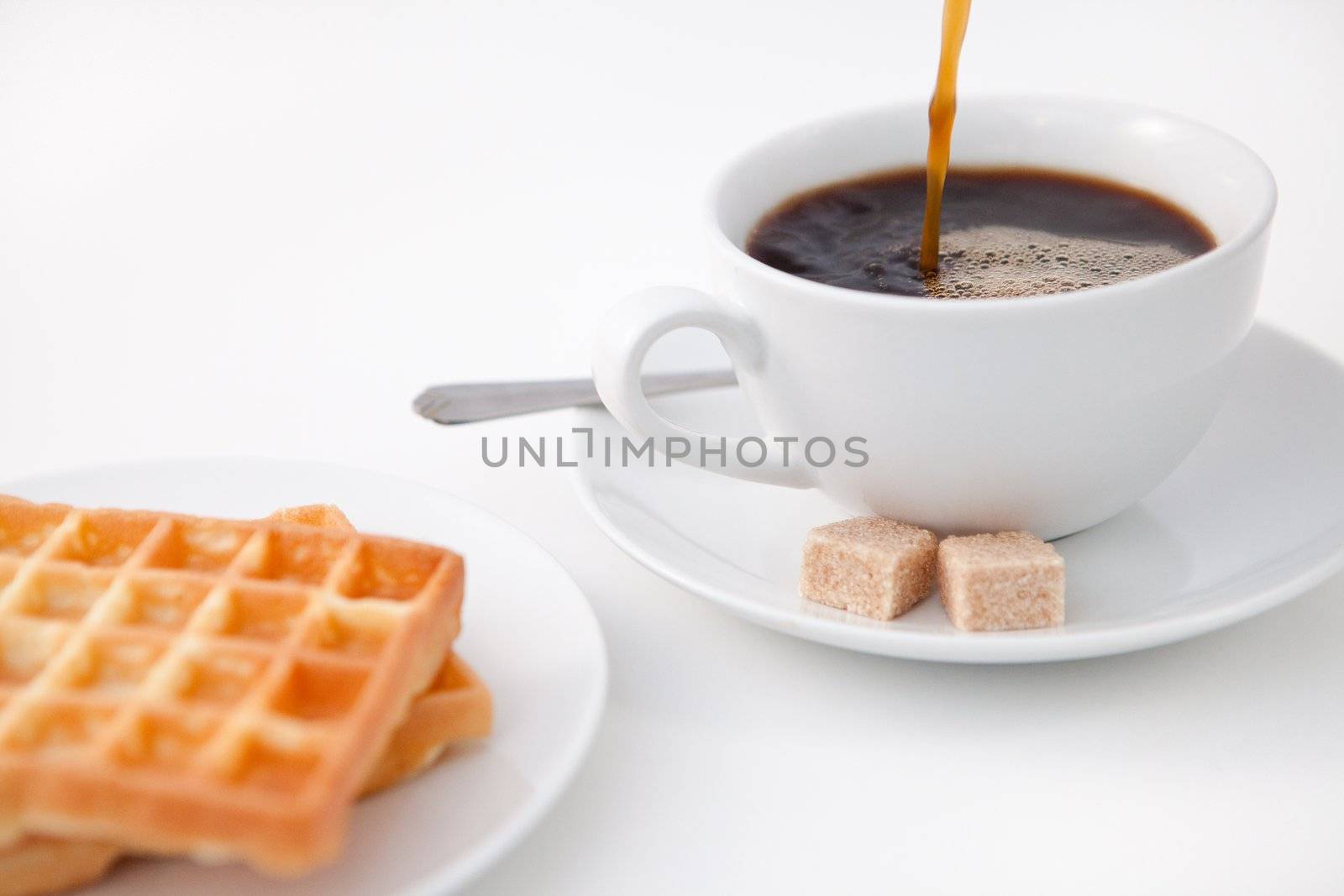 Waffles sugar and a cup of coffee on white plate against a white background