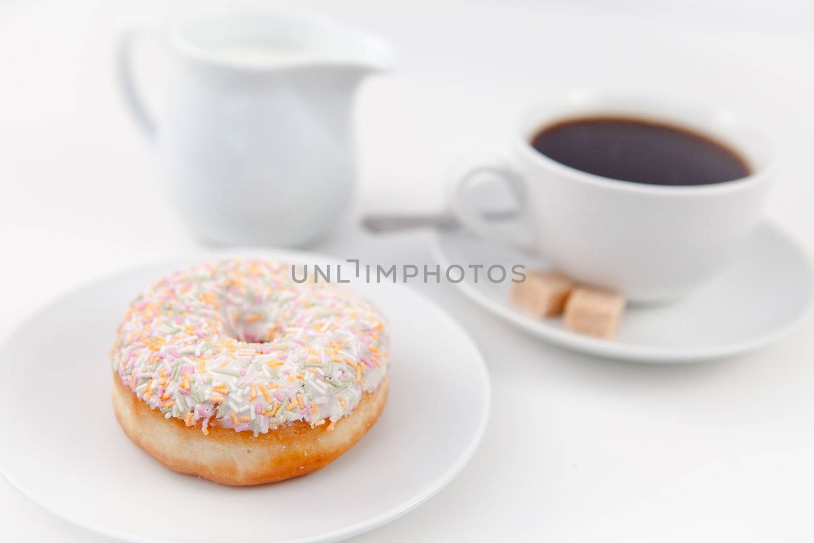 Milk and a cup of coffee on white plates with sugar and spoon against a white background