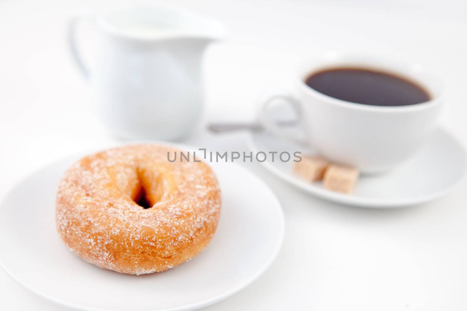 Doughnut with icing sugar and a cup of coffee on white plates with sugar and milk against a white background