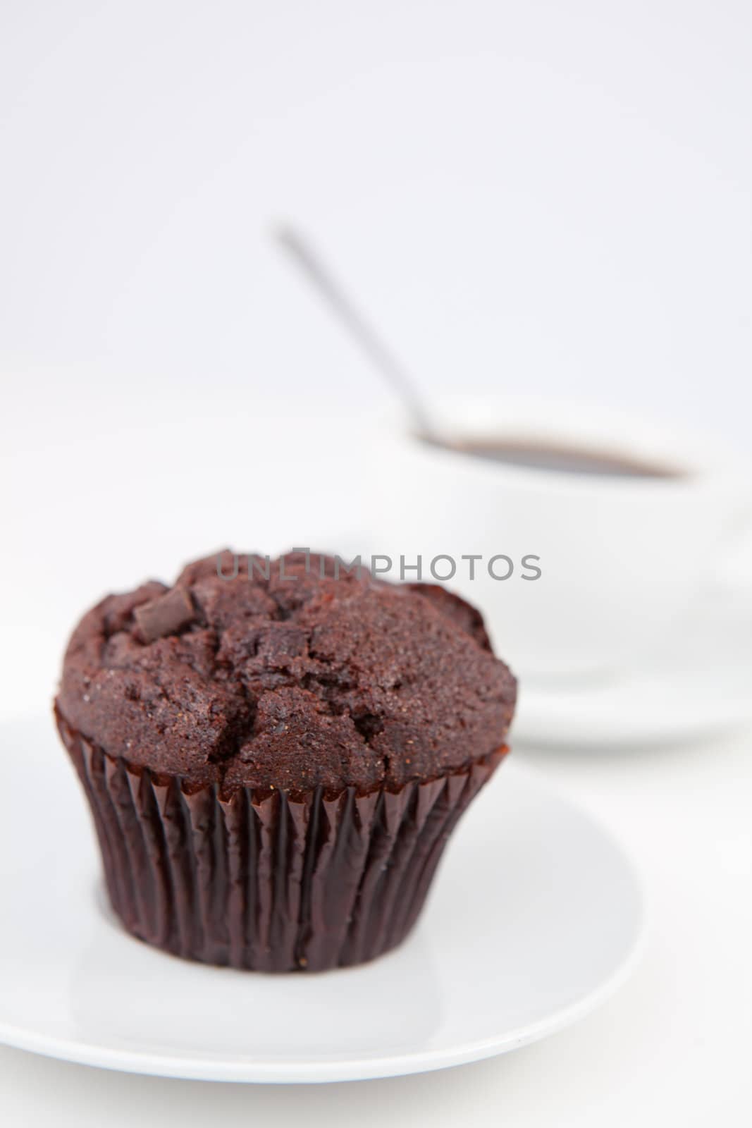 Chocolate muffin and a cup of coffee with a spoon on white plates against a white background