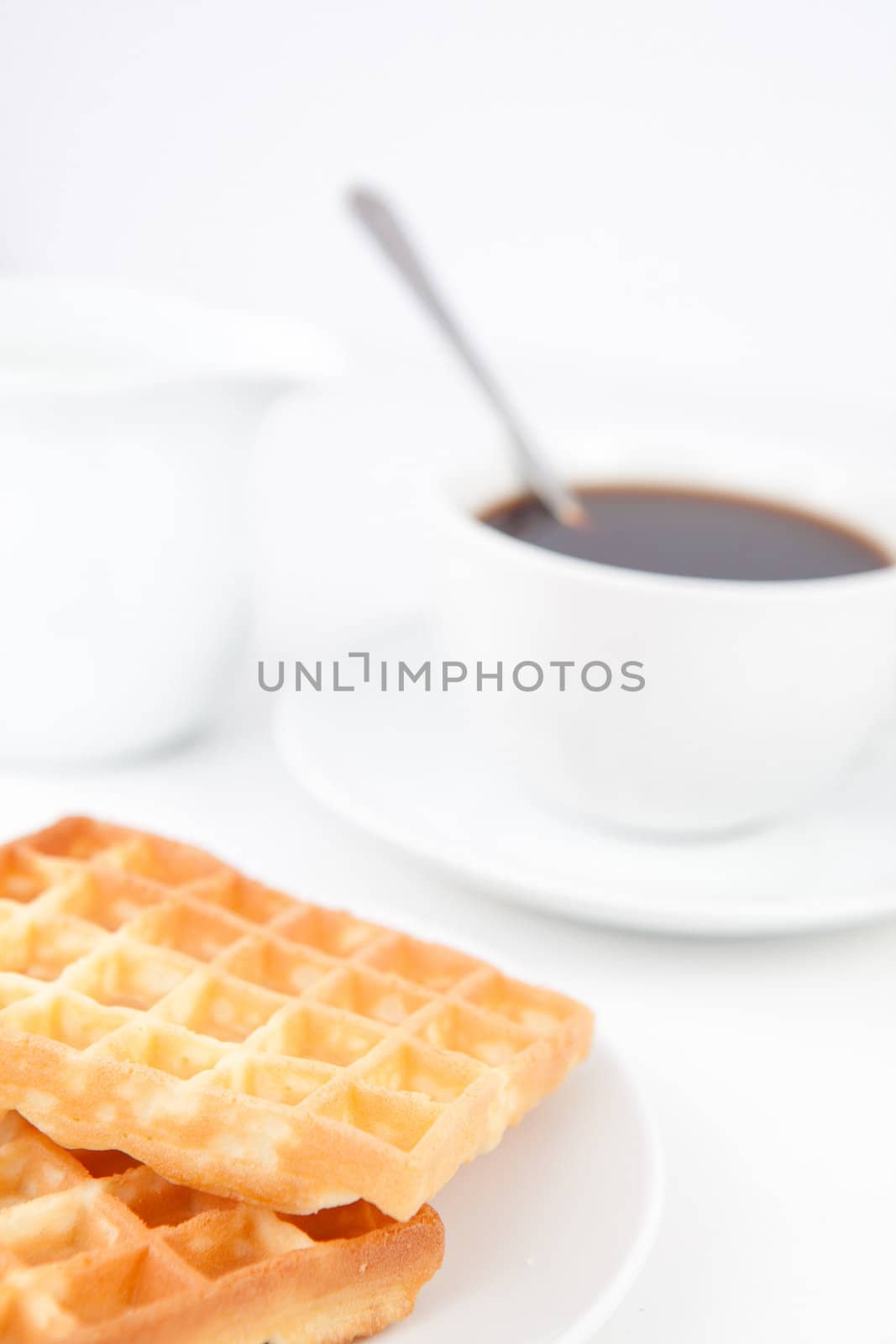 Waffles and a cup of coffee with a spoon on white plates and milk against a white background