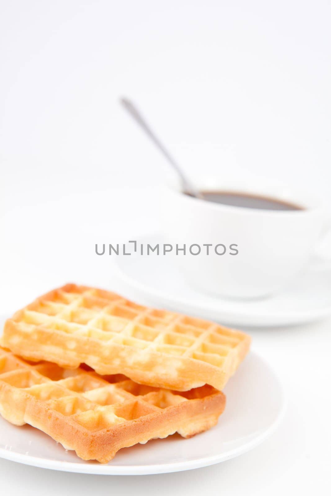 Waffles and a cup of coffee with a spoon on white plates against a white background