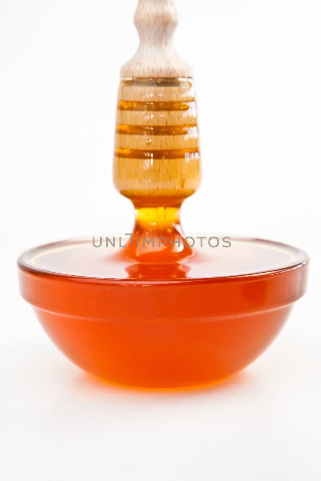 Honey trickle vertically dropping in full honey bowl against a white background