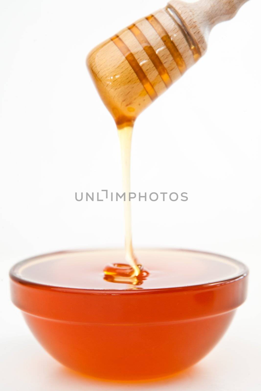 Honey trickle dropping in bowl against a white background