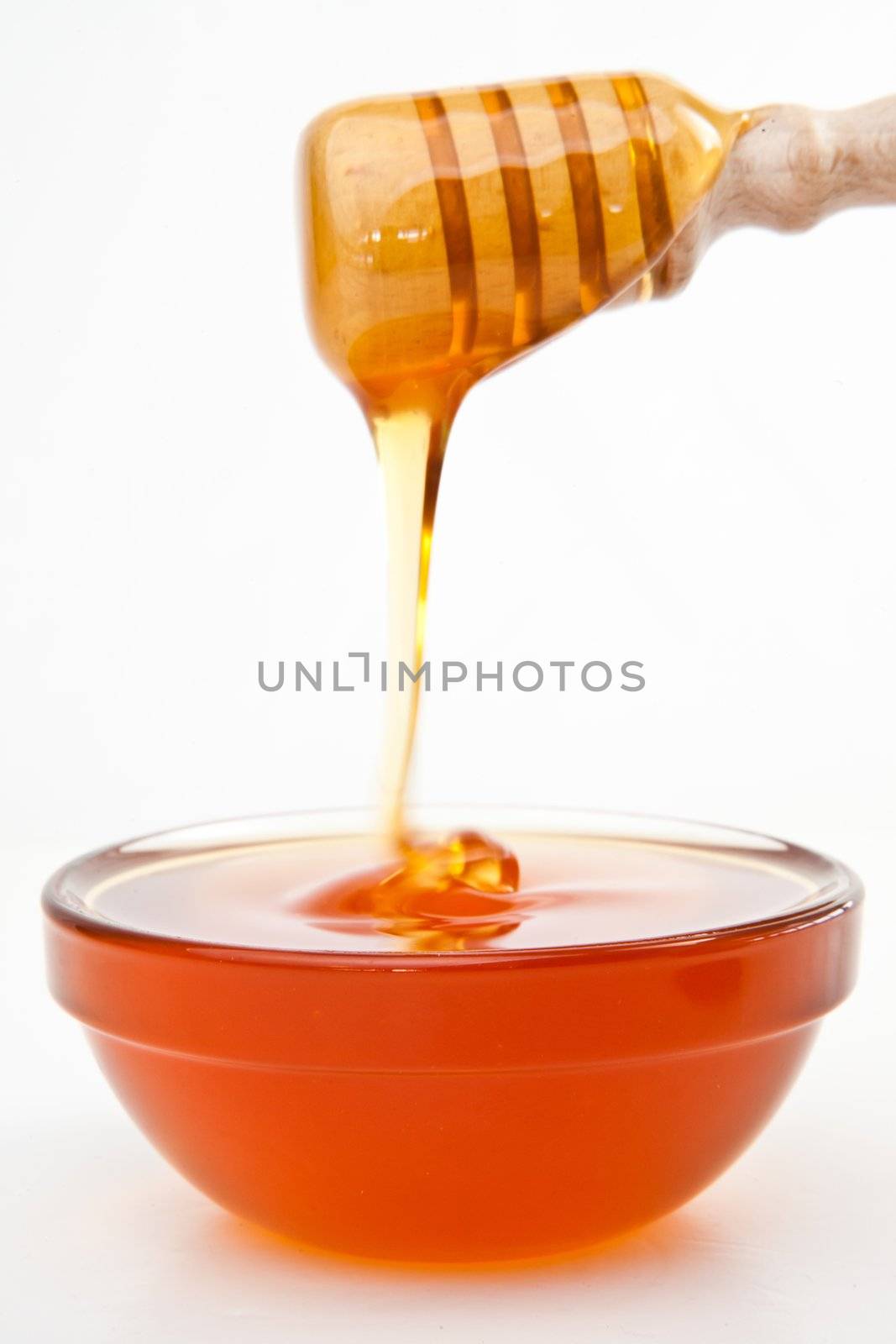 Honey on a honey dipper dropping in a bowl against a white background