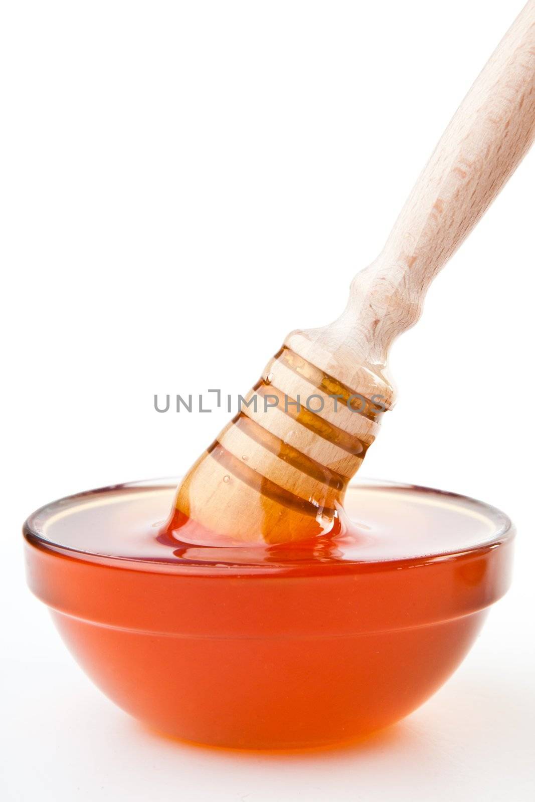 Honey dipper to the surface on  the honey bowl against a white background