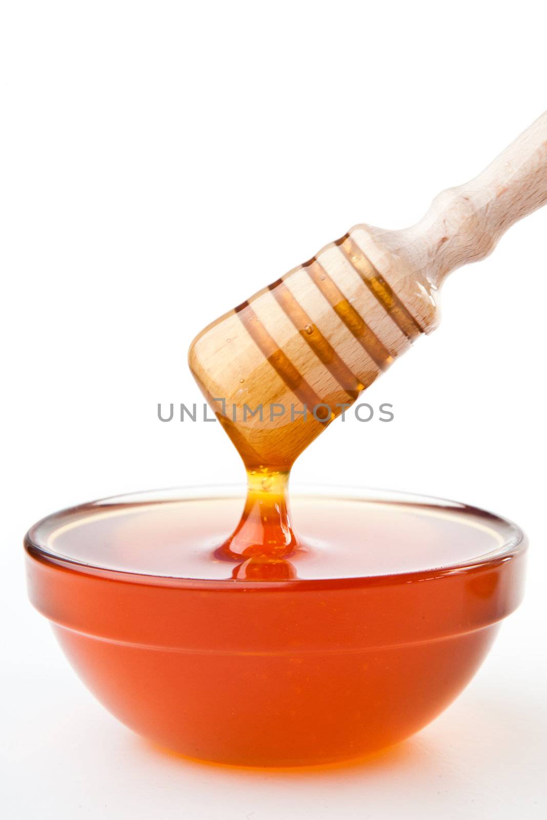 Honey dipper on top of a honey bowl against a white background