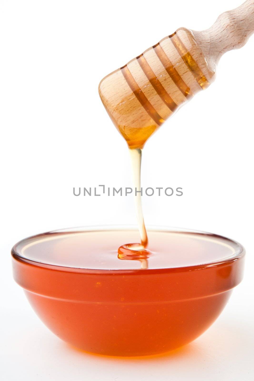 Honey sticky trickle dropping in bowl against a white background