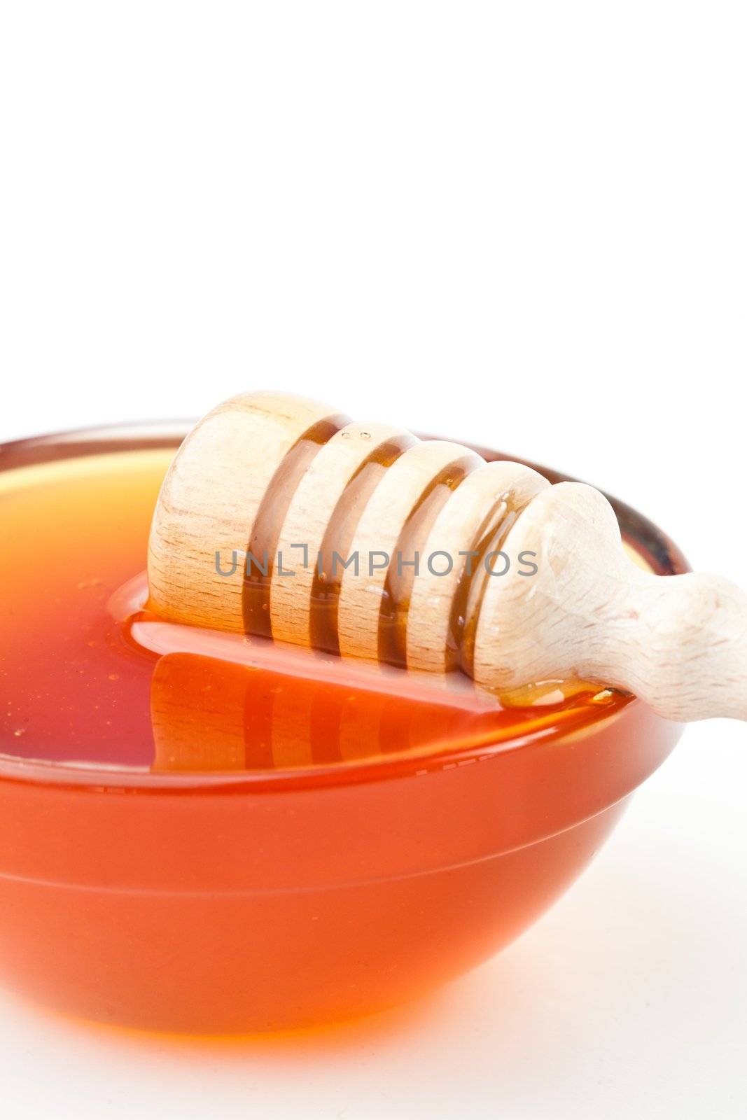 Honey dipper honrizontally on the edge of the bowl against a white background