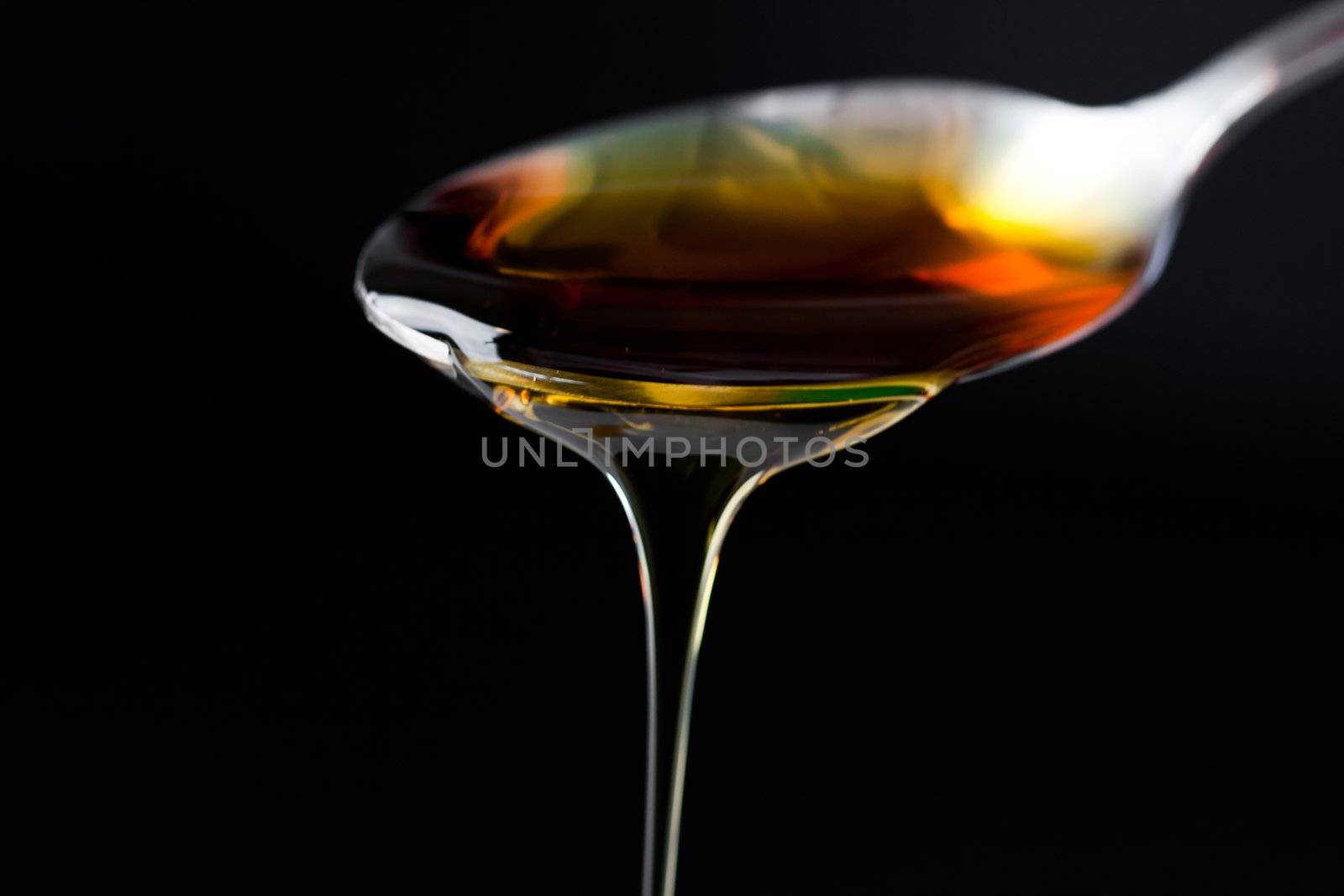 Honey trickle dropping of a full spoon against a black background