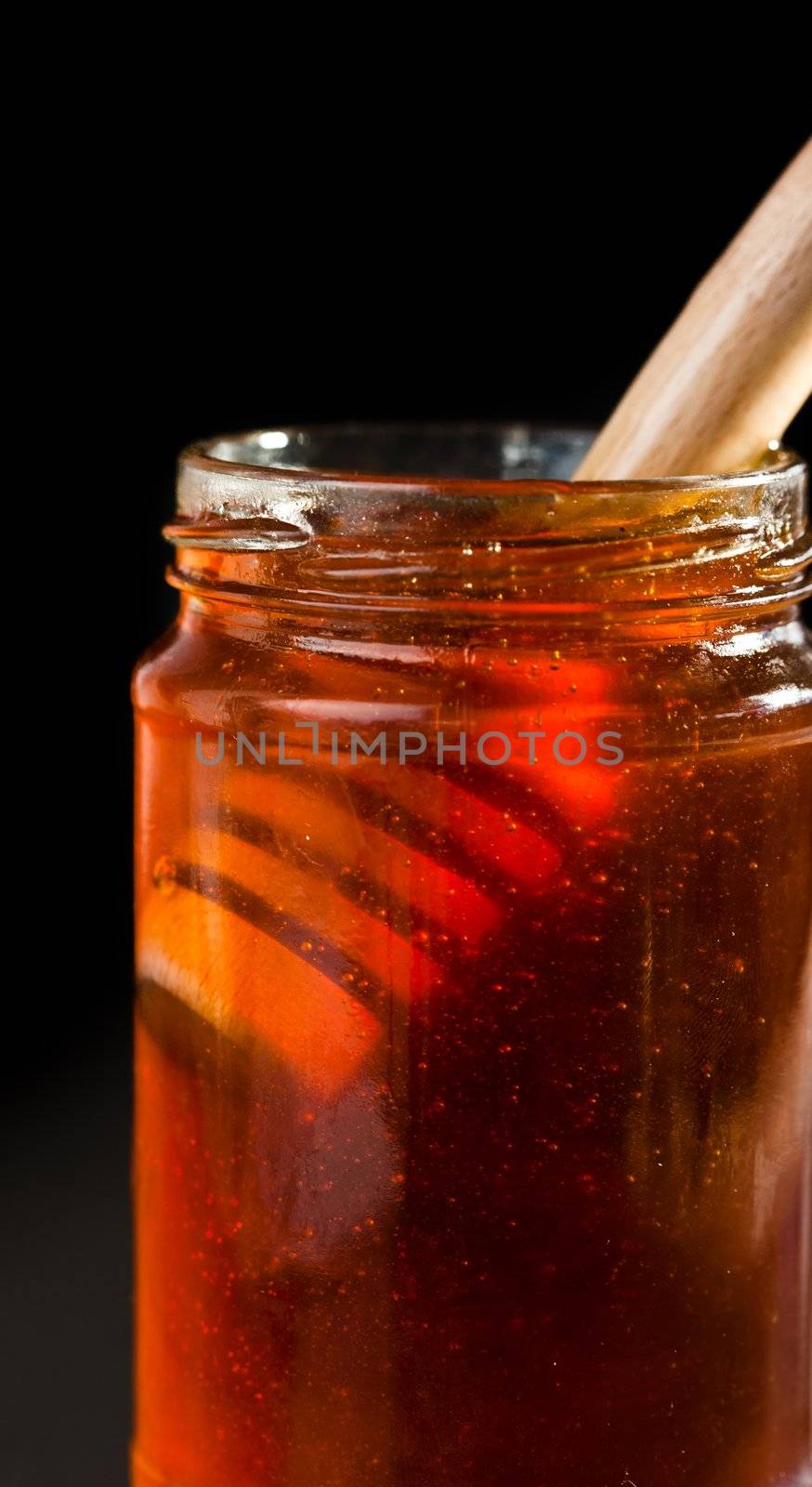 Close up of a honey jar with a honey dipper against a black bakground