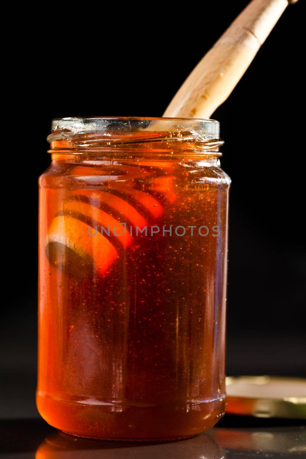 Honey full jar with a honey dipper against a black background