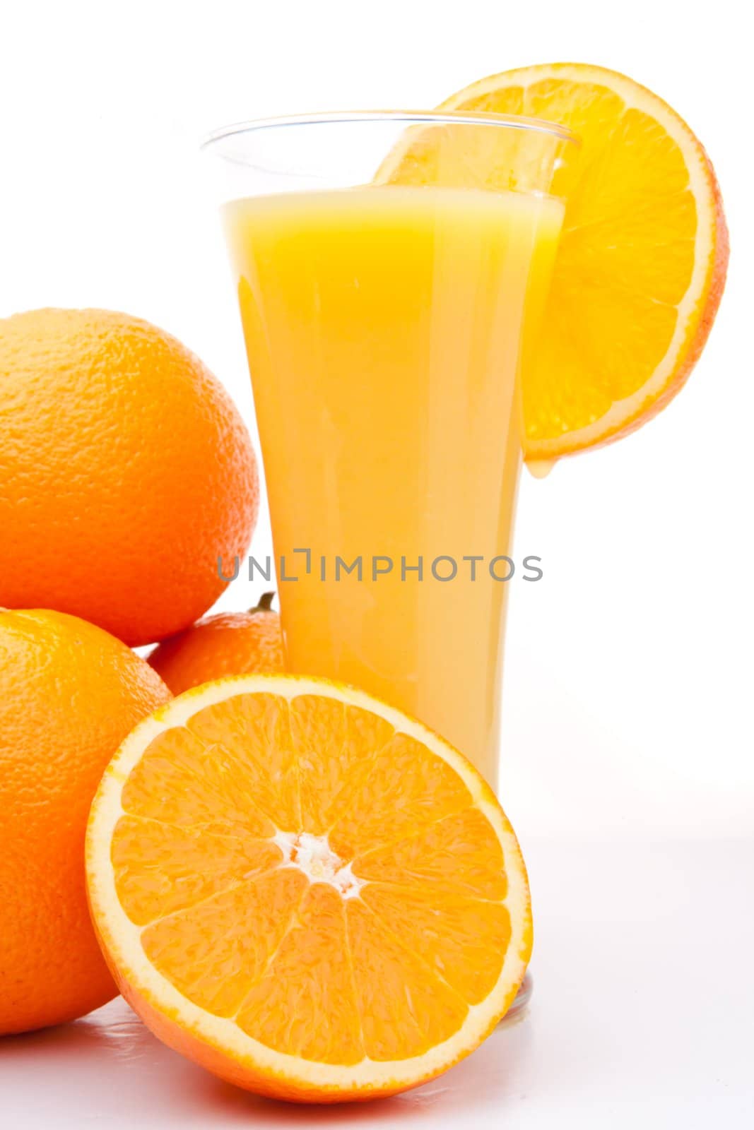 Pile of oranges near a glass of orange juice against white background