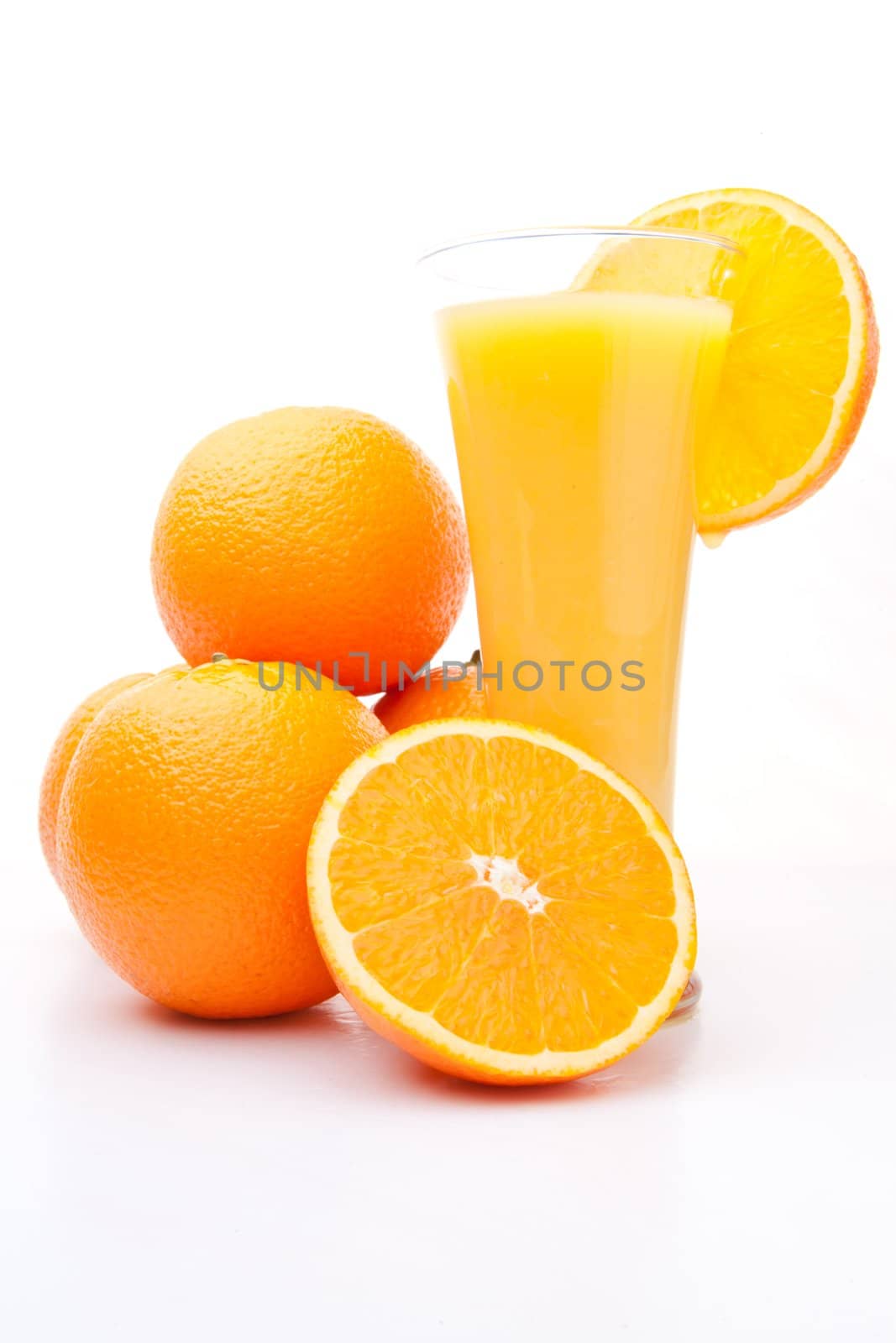 Heap of oranges near a glass of orange juice against white background