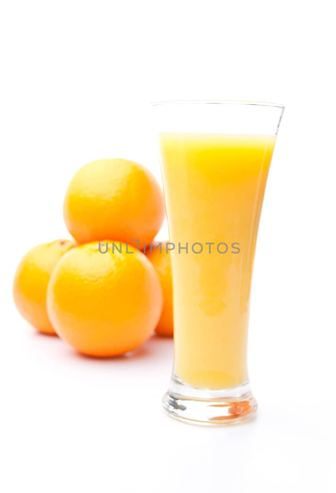 Heap of oranges behind a glass of orange juice against white background