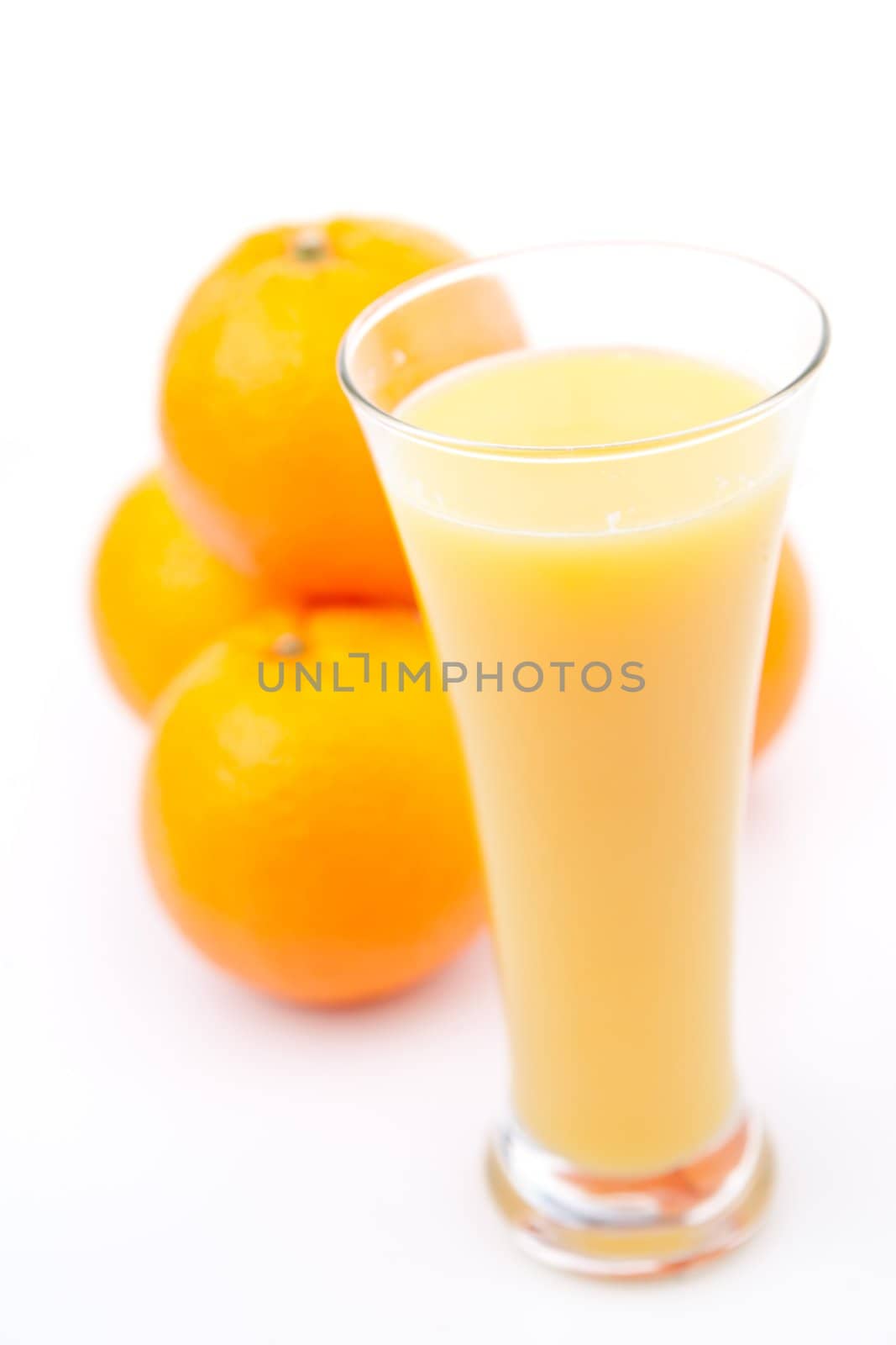 Oranges behind a glass of orange juice against white background