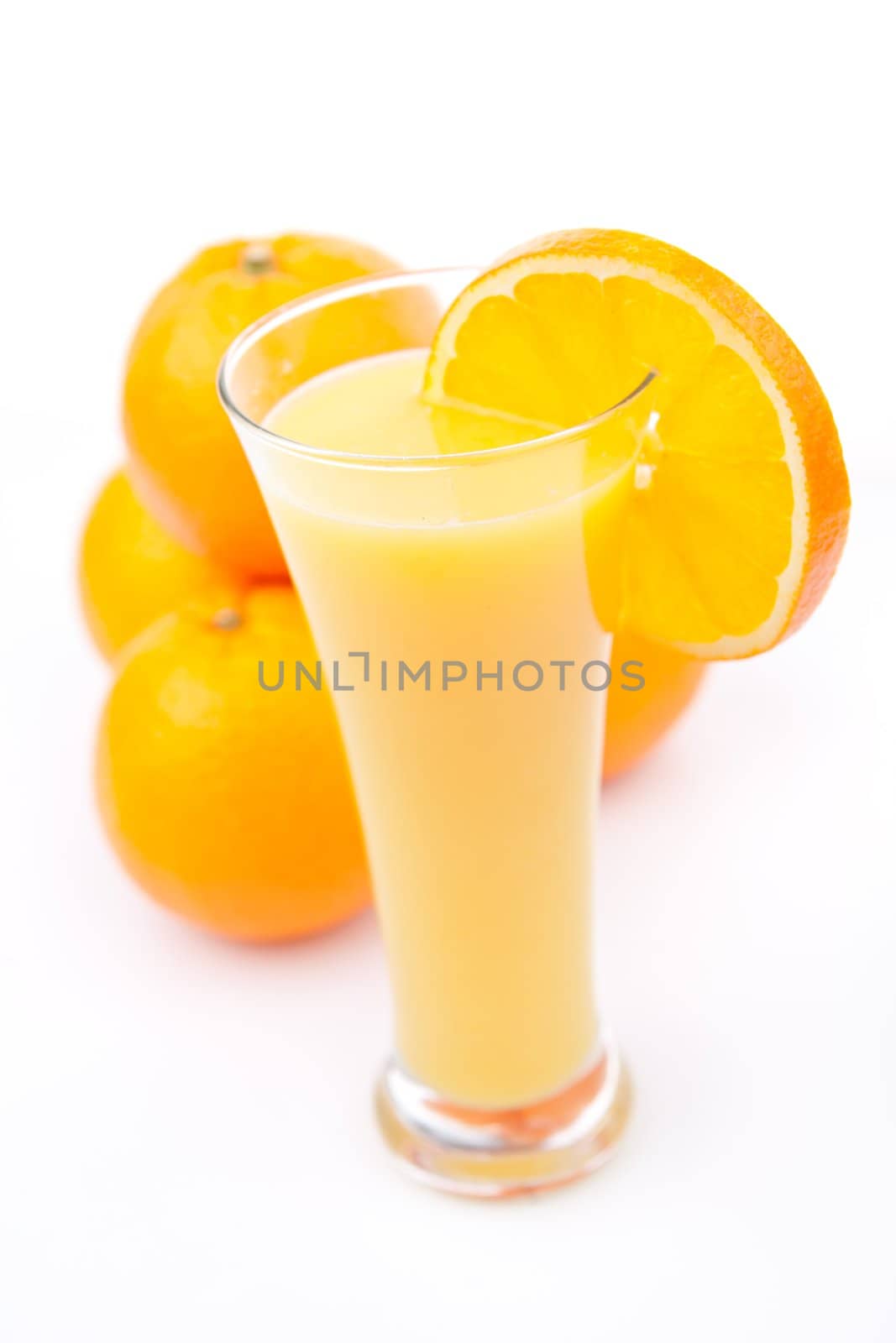 Full glass of orange juice placed near a heap of oranges against whitebackground