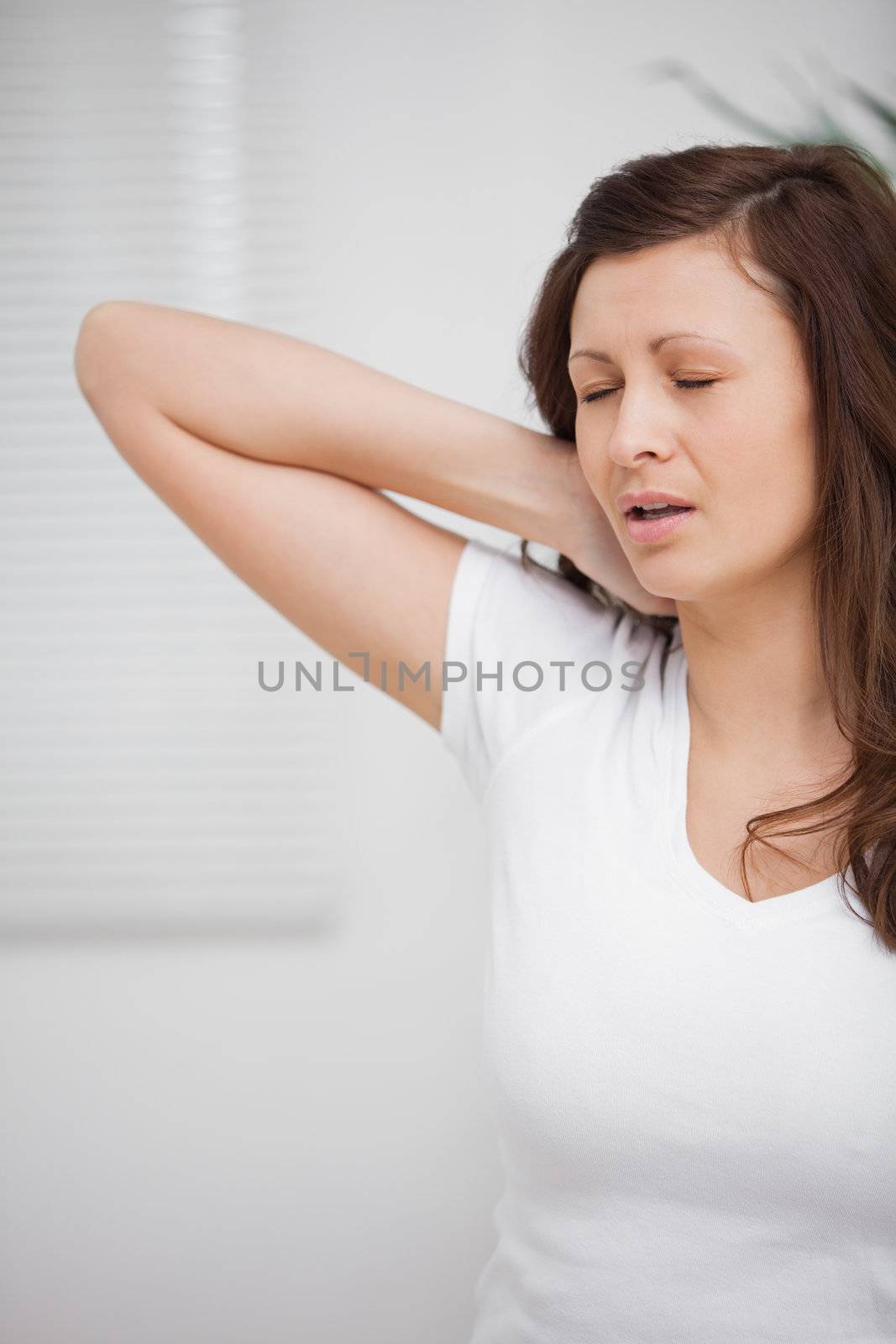 Woman touching her painful neck in a room
