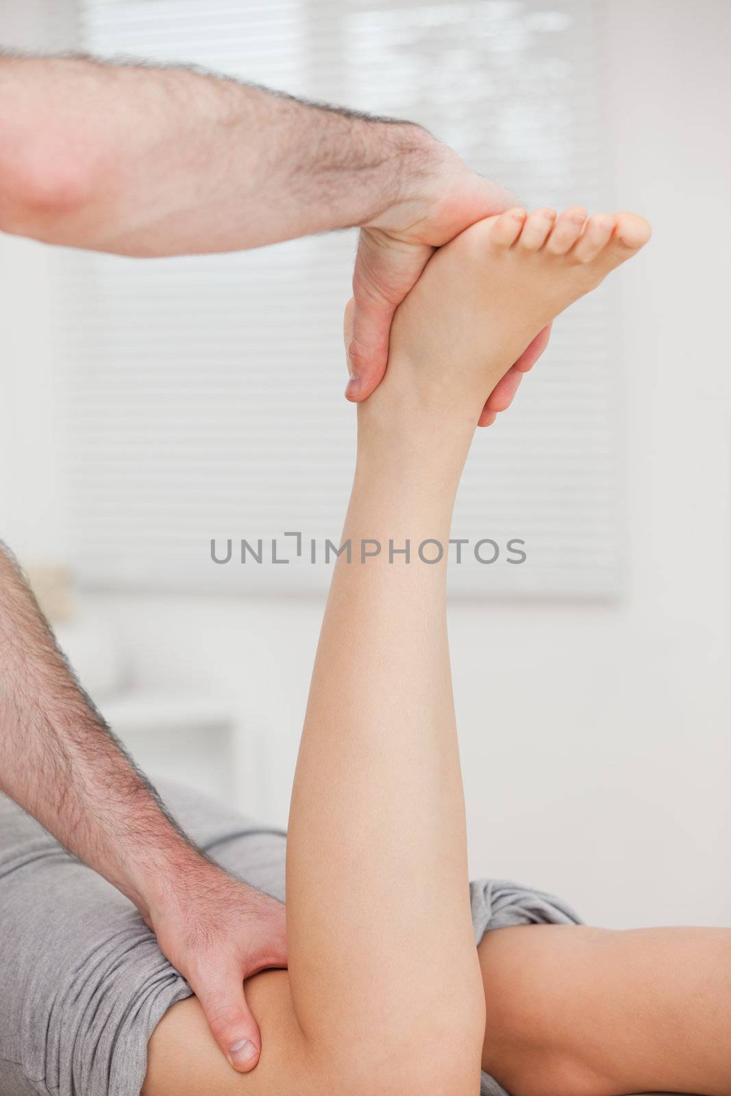Woman lying forward while her doctor is manipulating her leg indoors