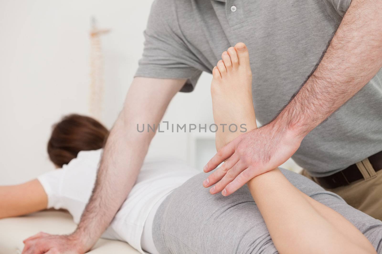 Physiotherapist bending the leg of his peaceful patient in a room