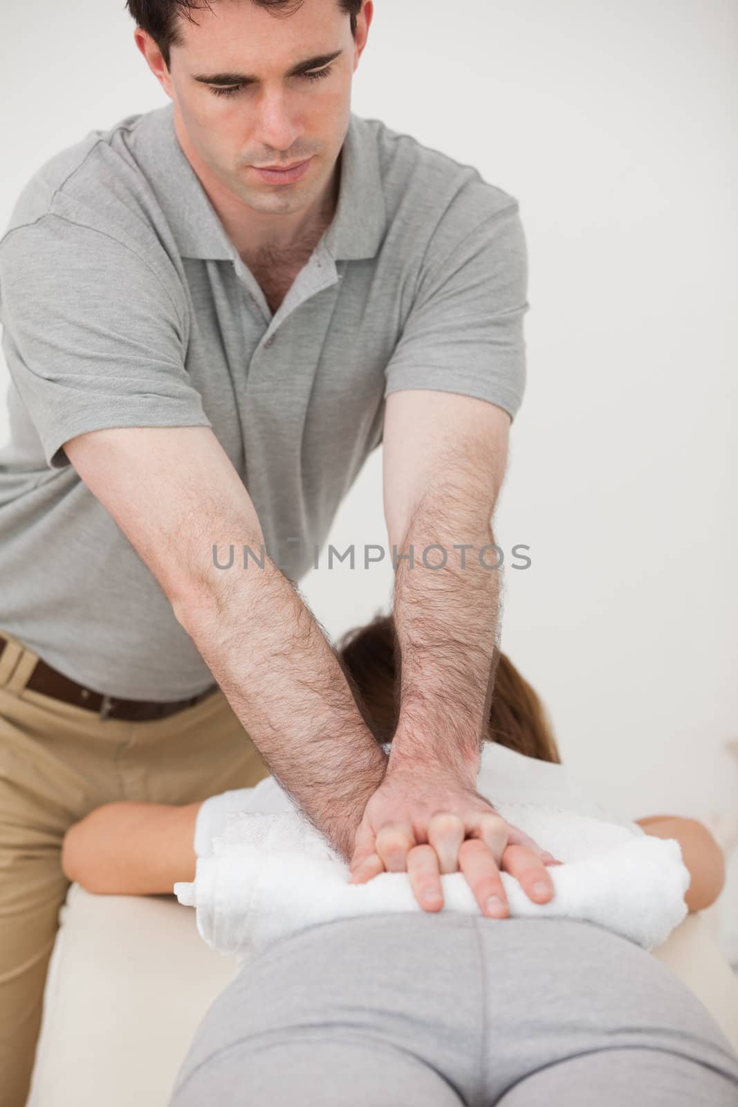 Woman lying forward while a physiotherapist massaging her back in a room