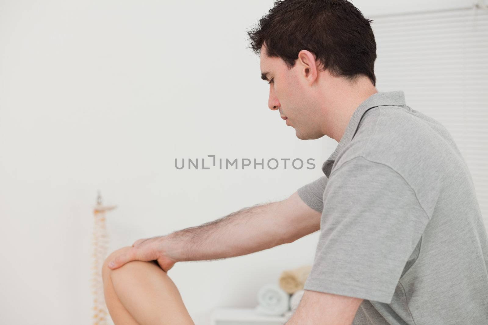 Serious chiropractor holding the knee of a patient by Wavebreakmedia