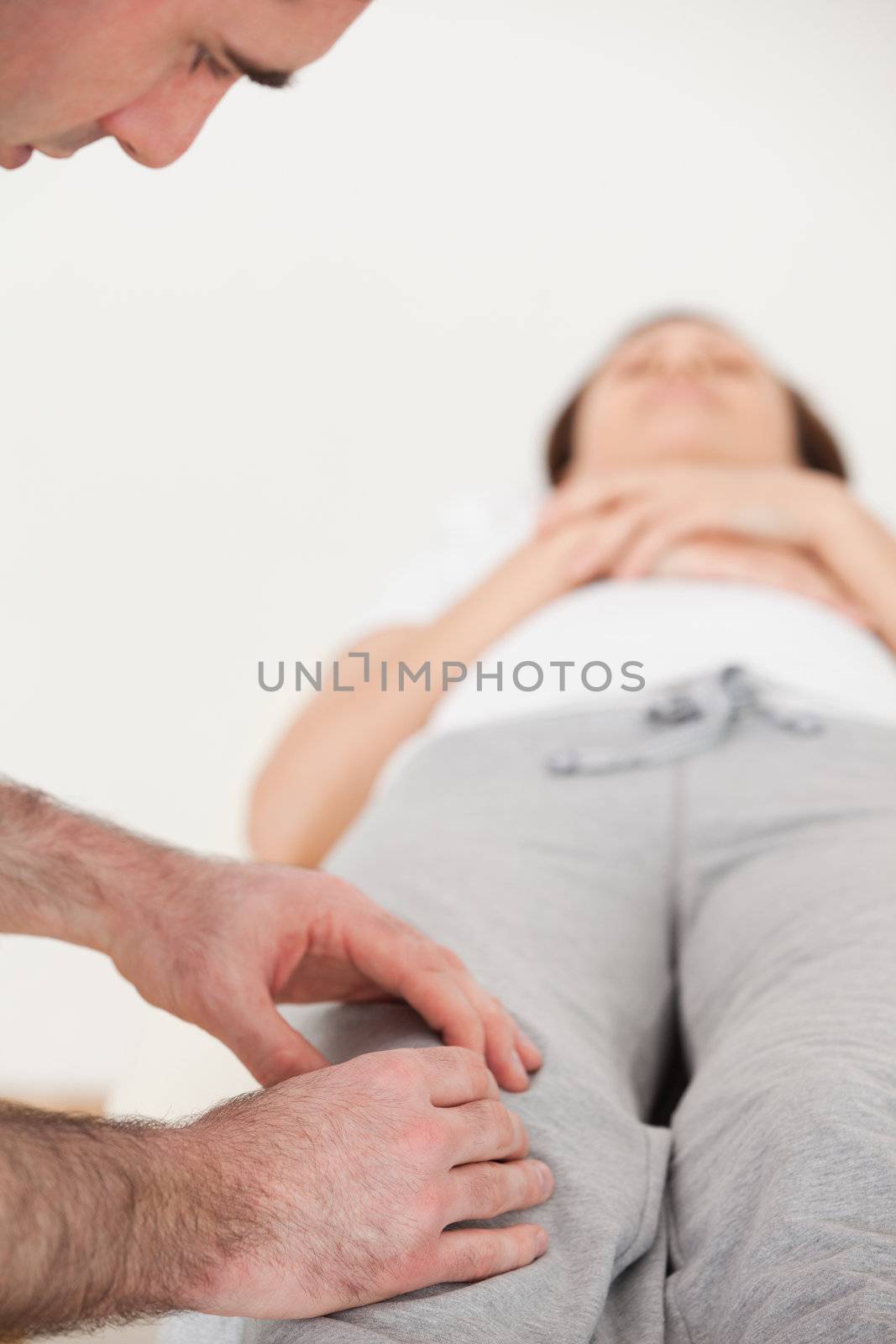 Woman lying on her back while a physiotherapist massing her knee by Wavebreakmedia