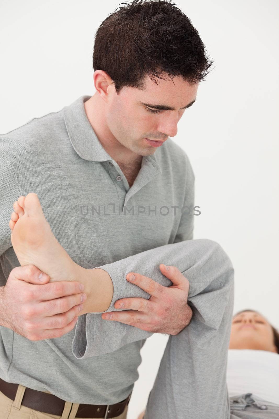 Chiropractor holding the leg of his patient while moving it in a room