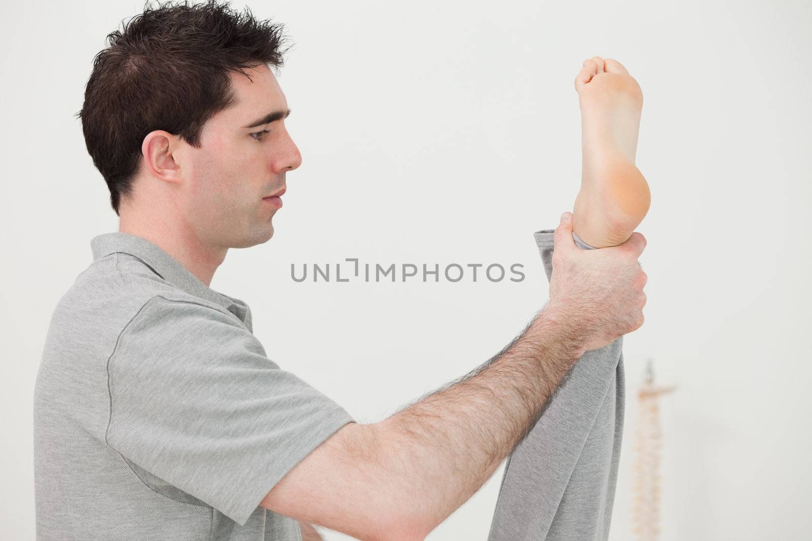 Brown-haired chiropractor stretching the leg of his patient in a room