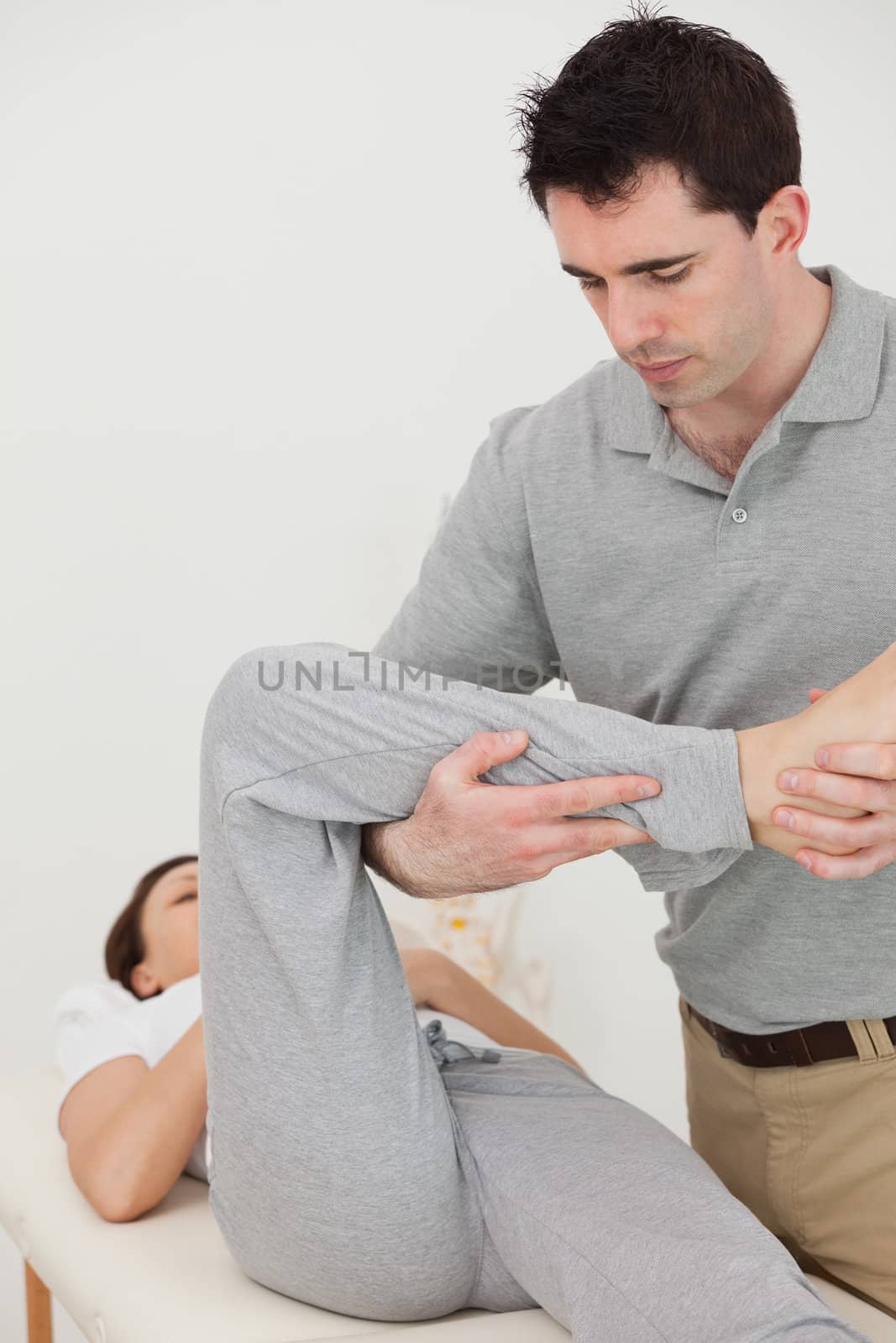 Brunette physiotherapist stretching the leg of a patient in his bright room