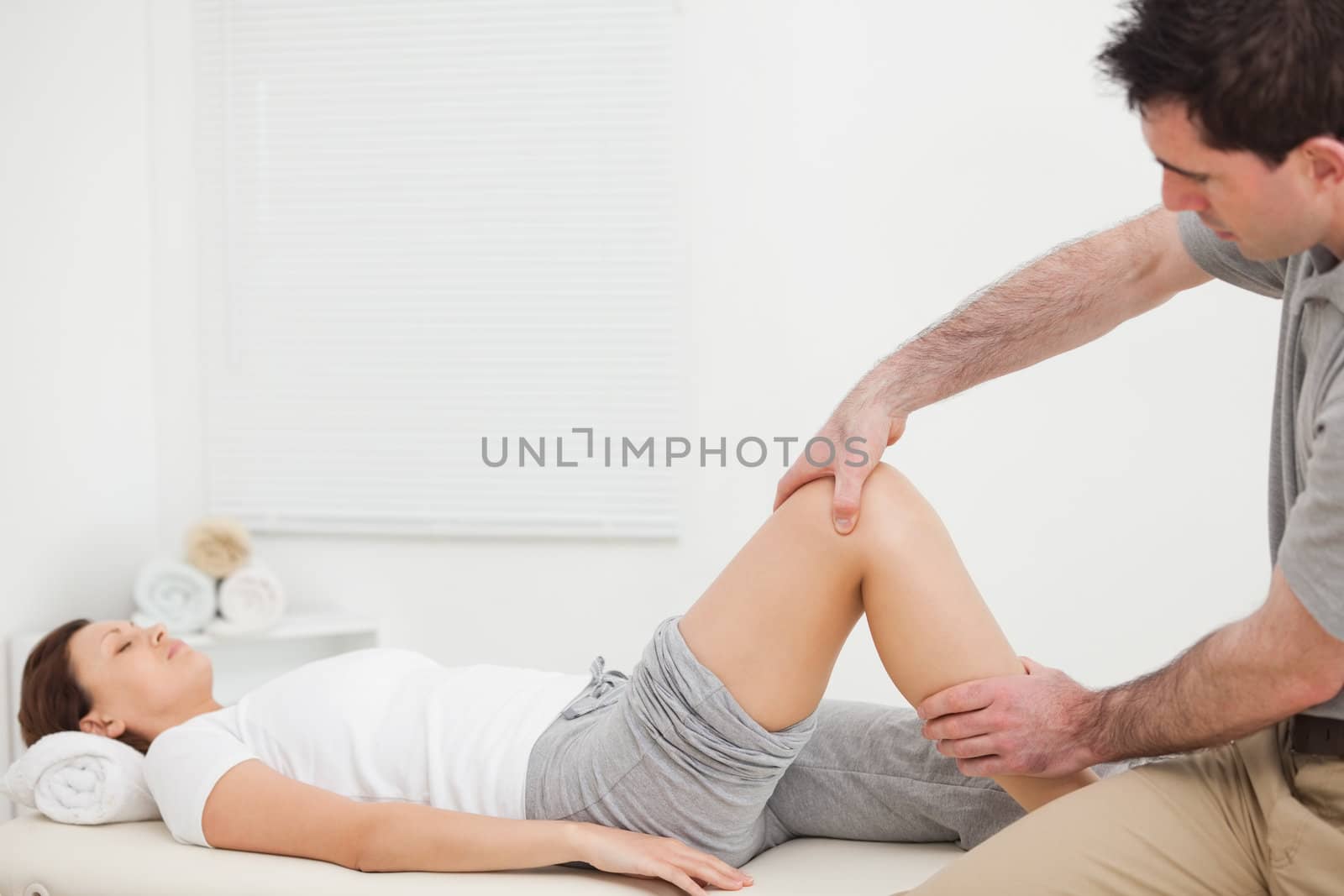 Brunette woman lying while a physiotherapist manipulates her leg indoors