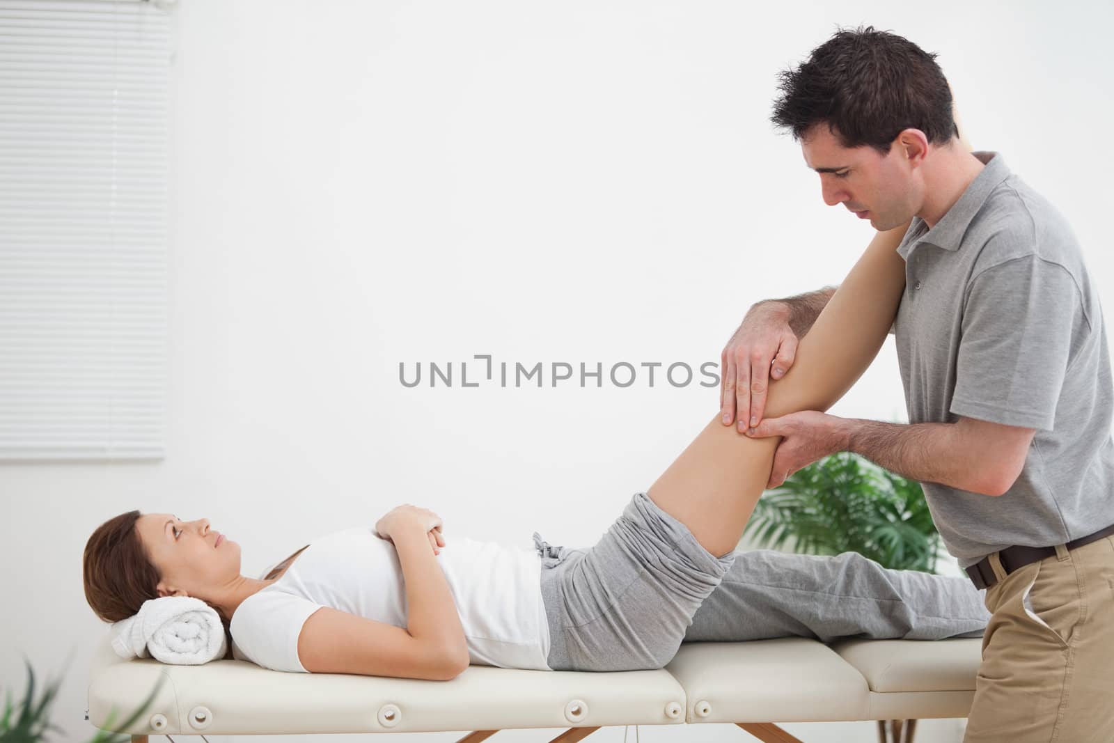 Physiotherapist massaging a leg while placing it on his shoulder in a room
