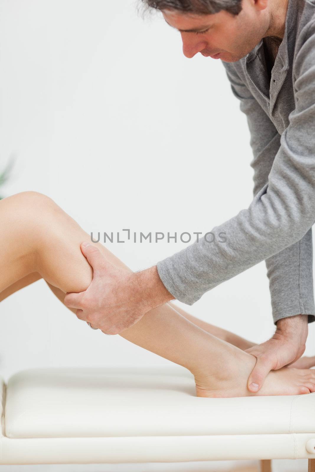 Serious osteopath holding the calf of a patient in a medical room