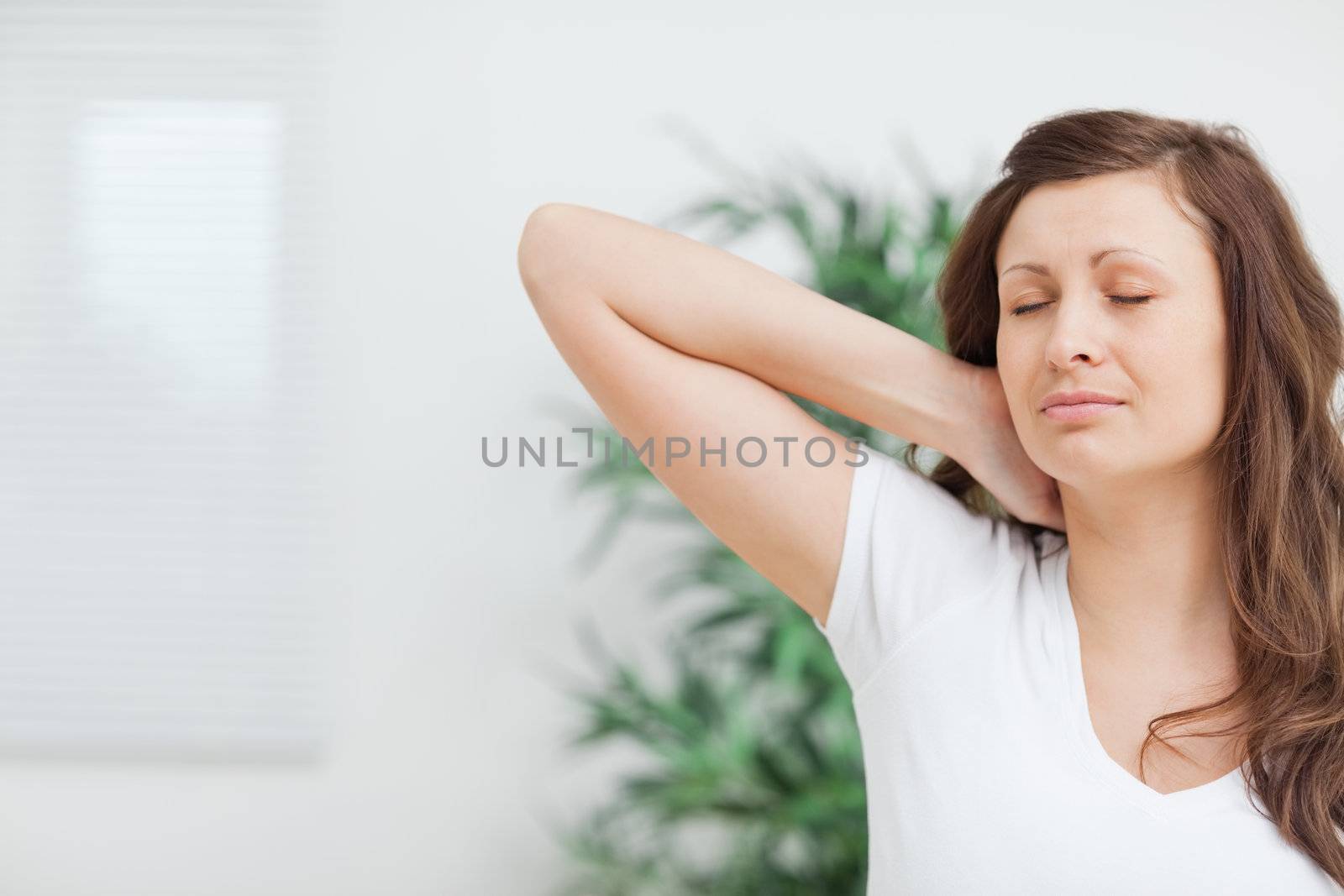 Woman placing her hand on her painful neck in a room