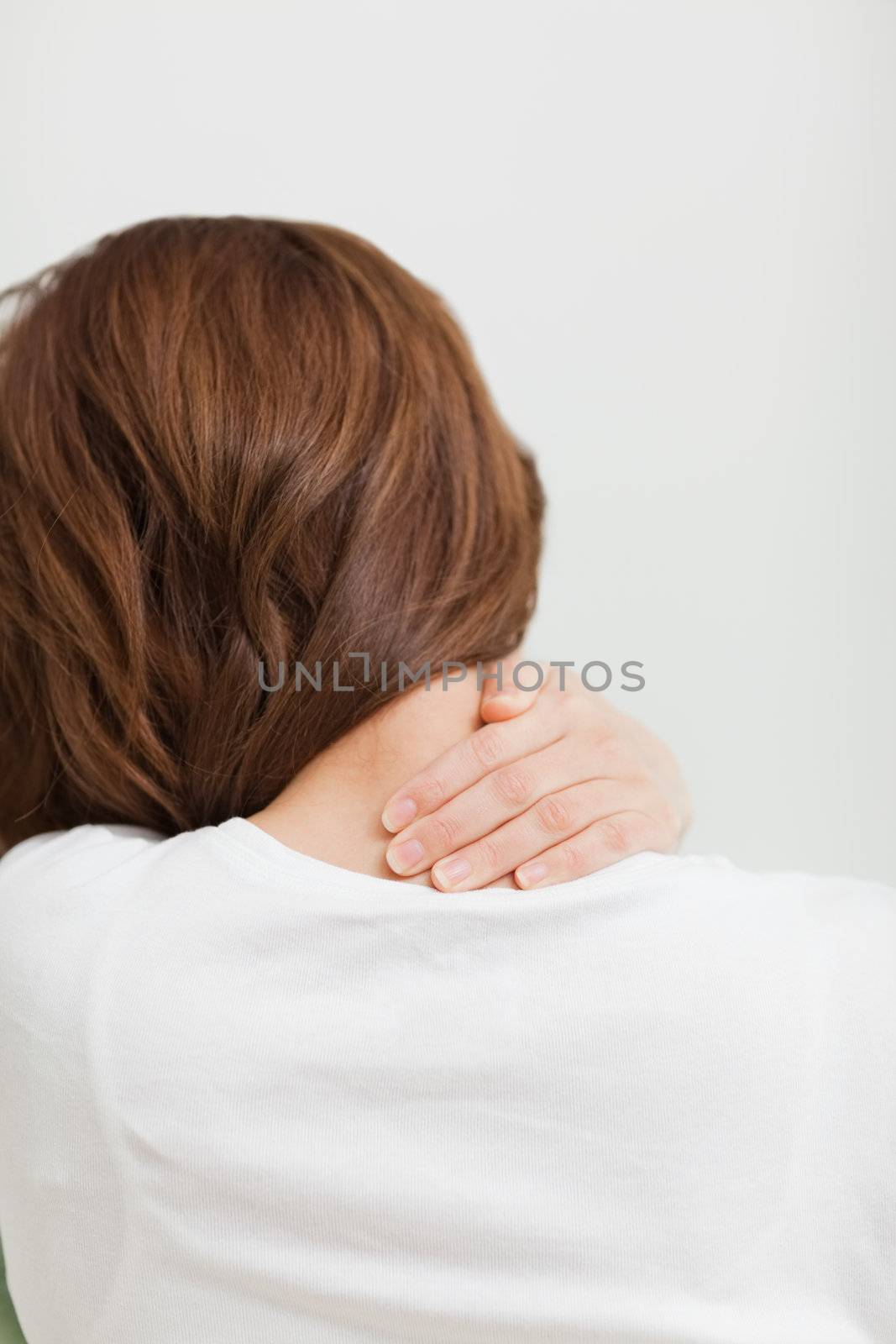 Brown-haired woman massaging her painful neck in a room