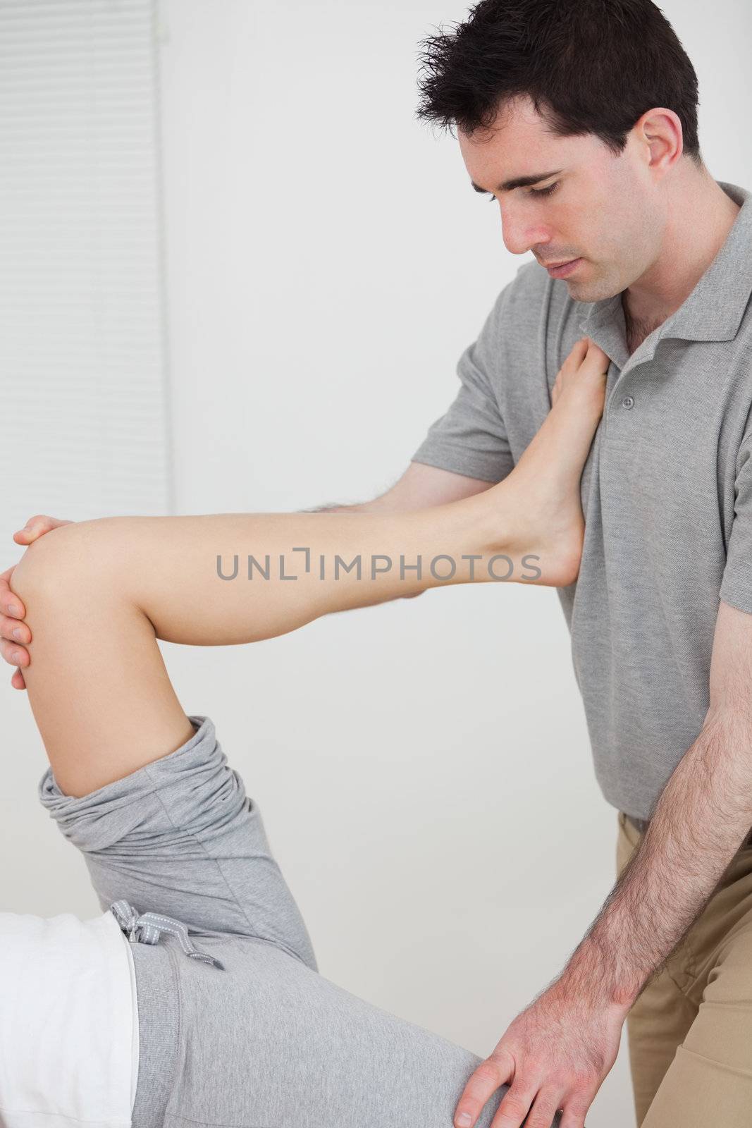 Physiotherapist stretching a leg while placed it on his chest in a room