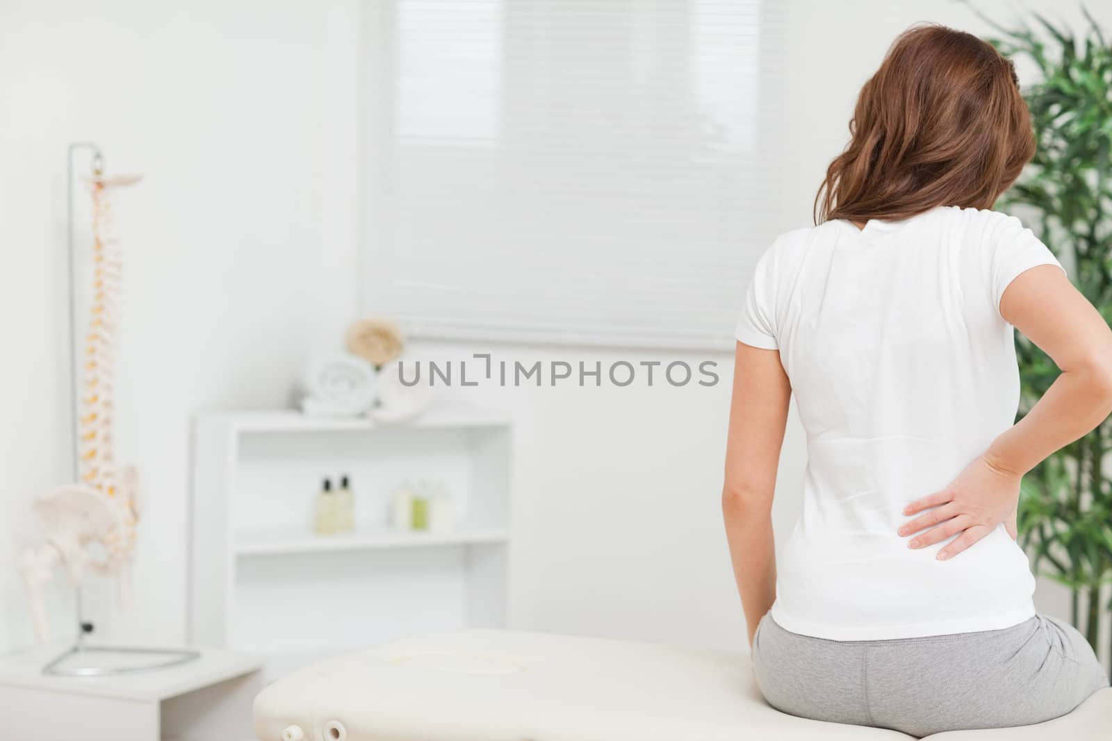 Woman sitting on a table while touching her back in a medical room