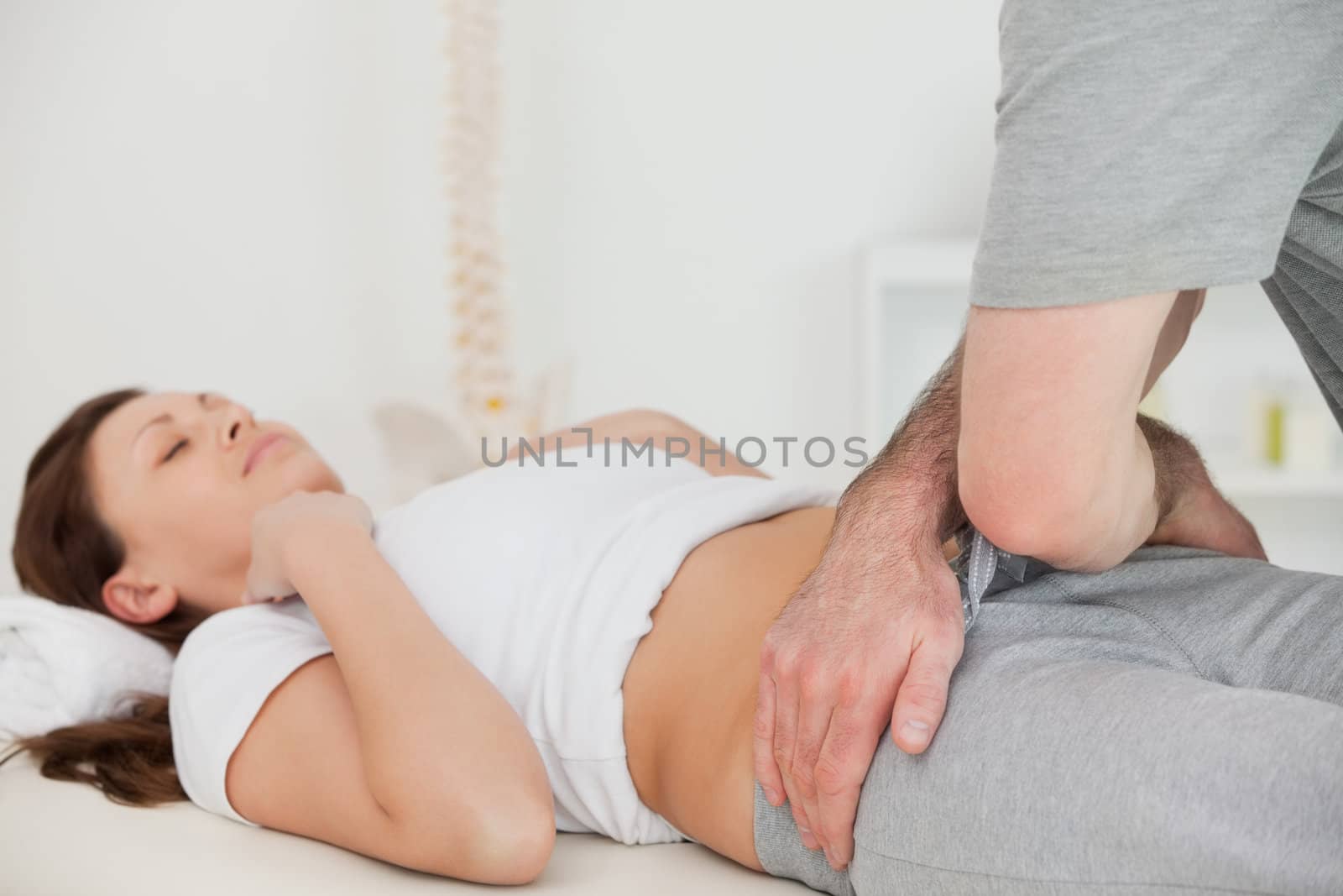 Brunette woman lying while a physiotherapist touching her hips in a room