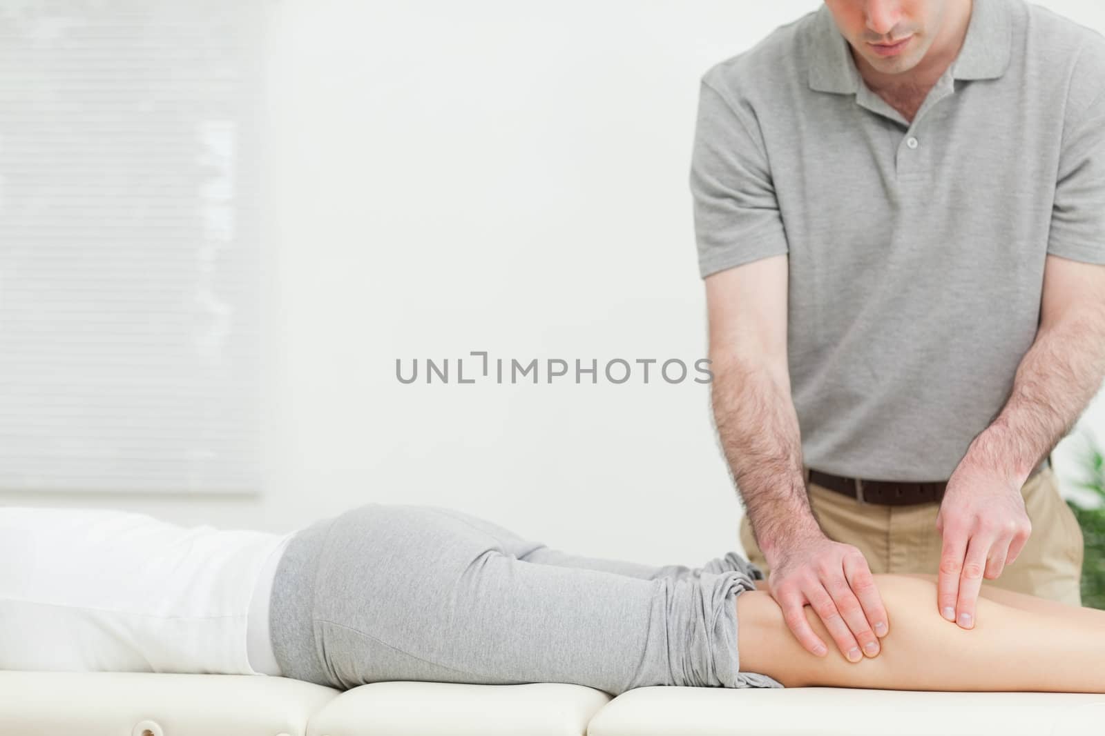 Woman lying forward while a physiotherapist massaging her leg in a room