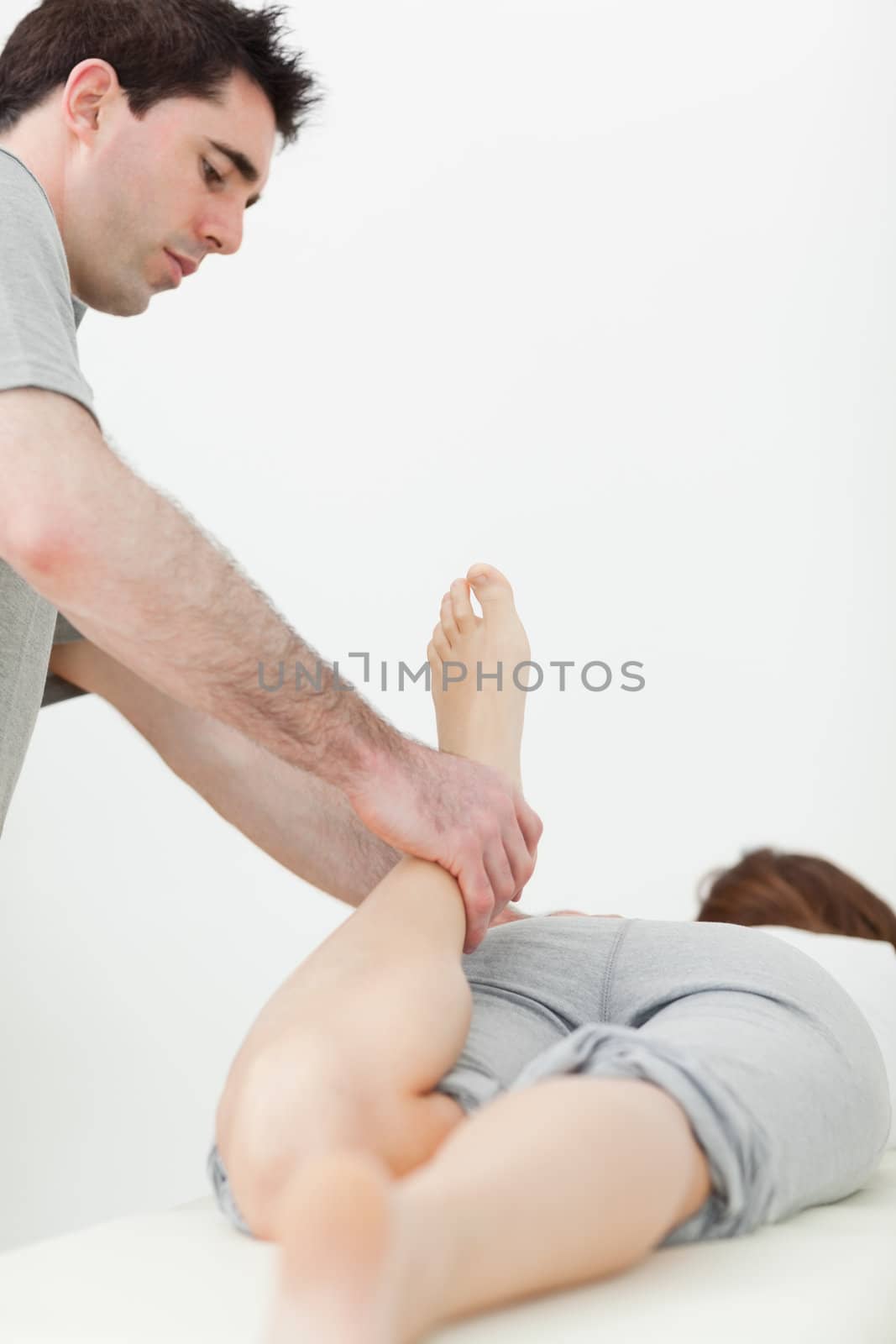 Serious physiotherapist manipulating the leg of a patient in a room