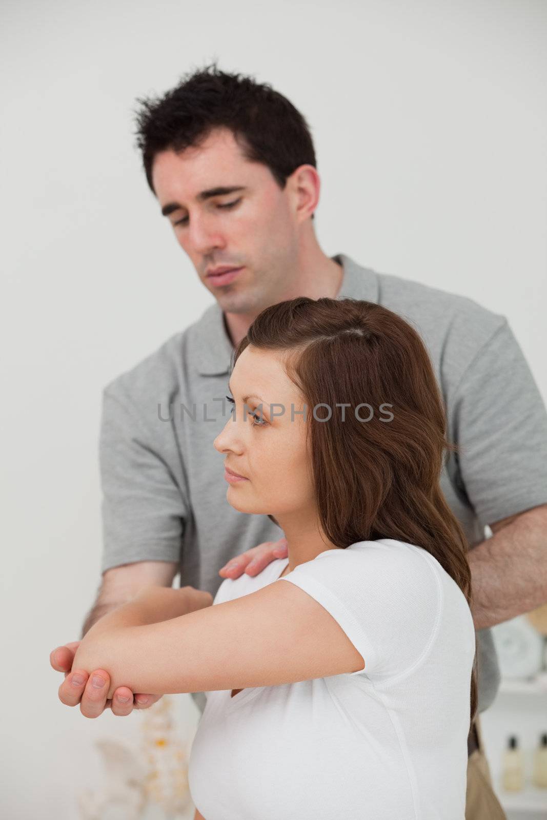Serious brunette doctor stretching the arm of a woman in a room