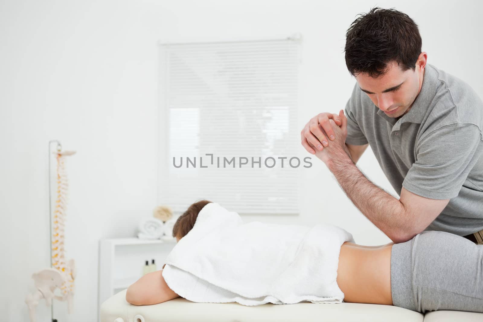Brunette physiotherapist massaging a woman with his elbow in a room