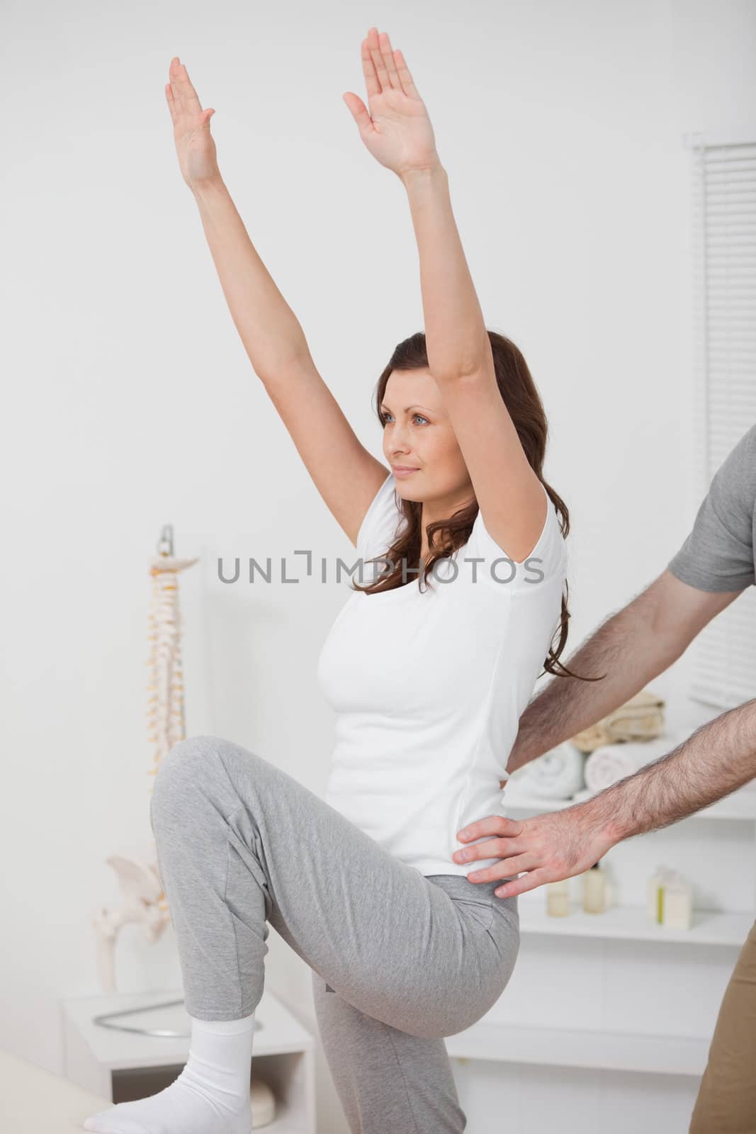 Woman doing exercise while a man is putting his hands on her hips in a room